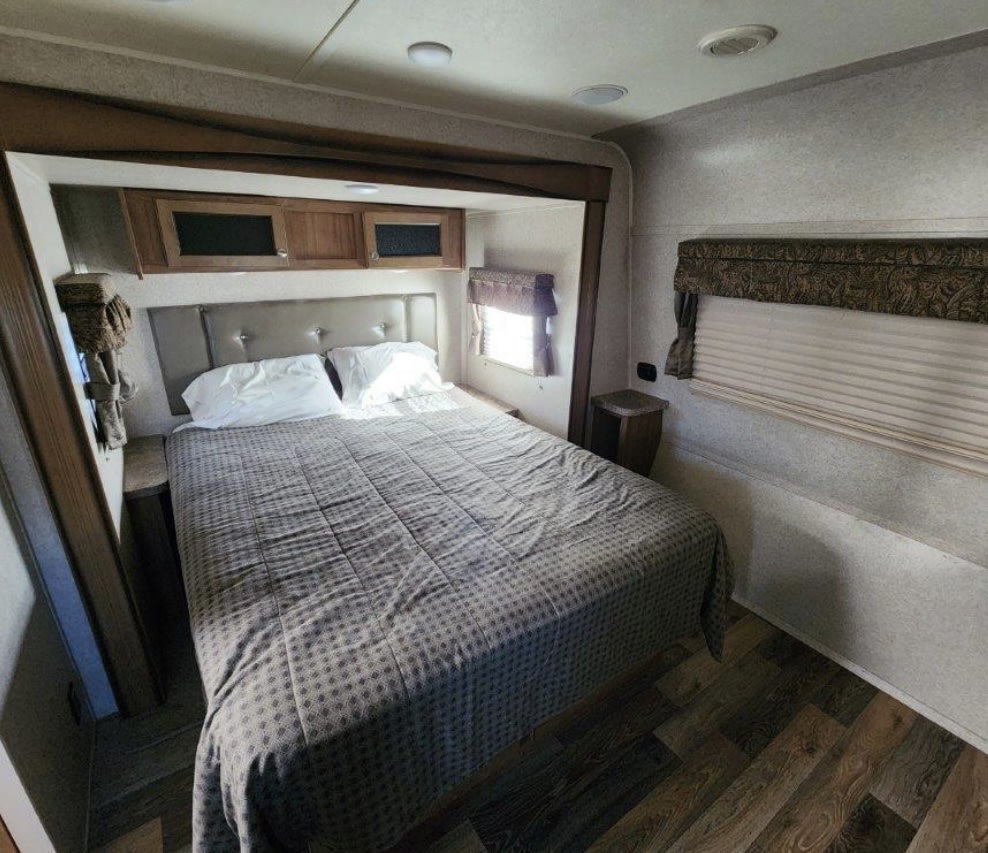 Relax in this RV rental bedroom: features a comfortable bed, overhead cabinets, window blinds, and wood-look flooring.. Forest River Rockwood Signature Ultra Lite 2017