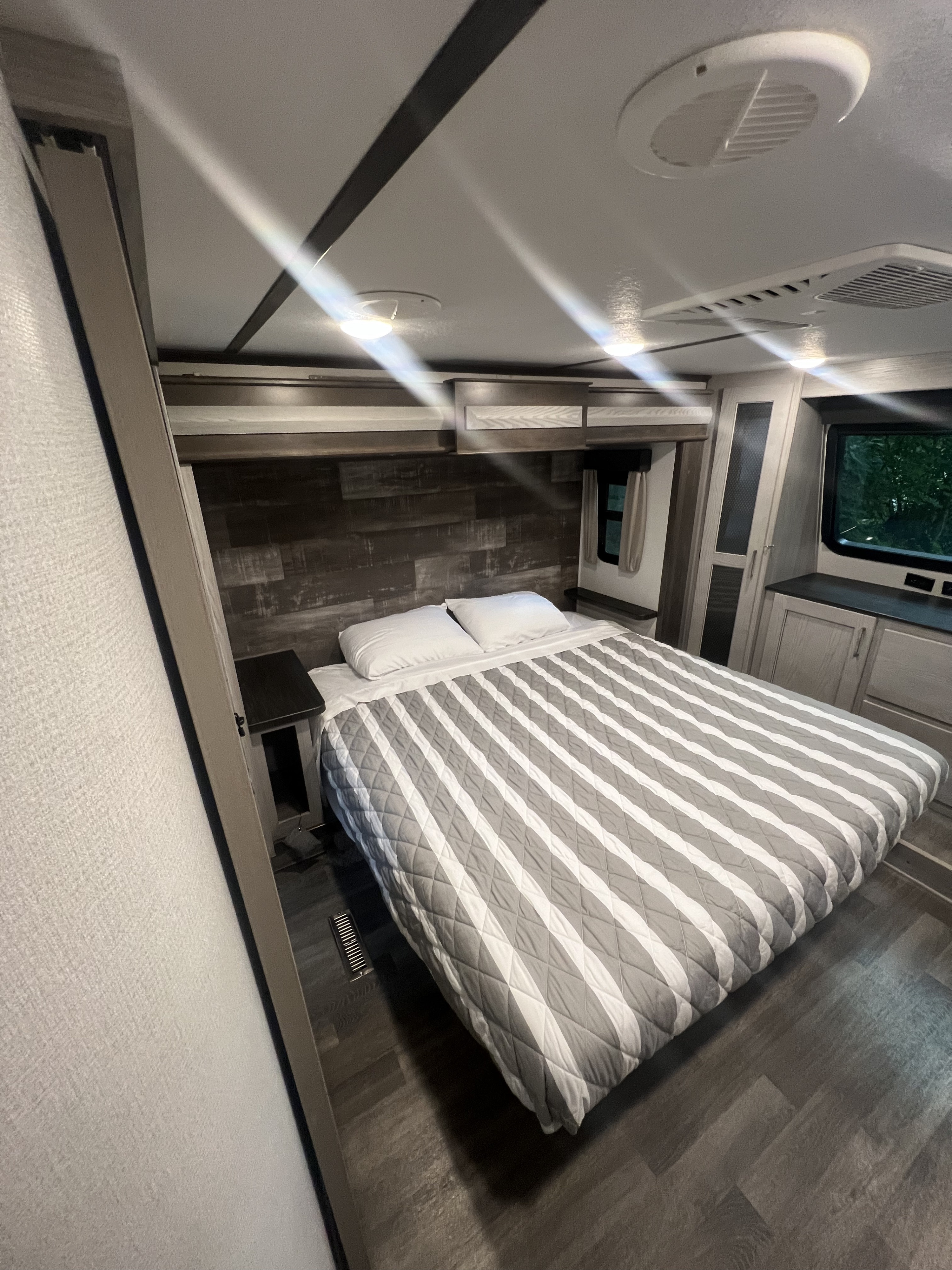 Inside an RV rental: a modern bedroom with a striped bed, wood headboard, and overhead lighting. Comfortable travel accommodations.. Keystone RV Montana High Country 2020