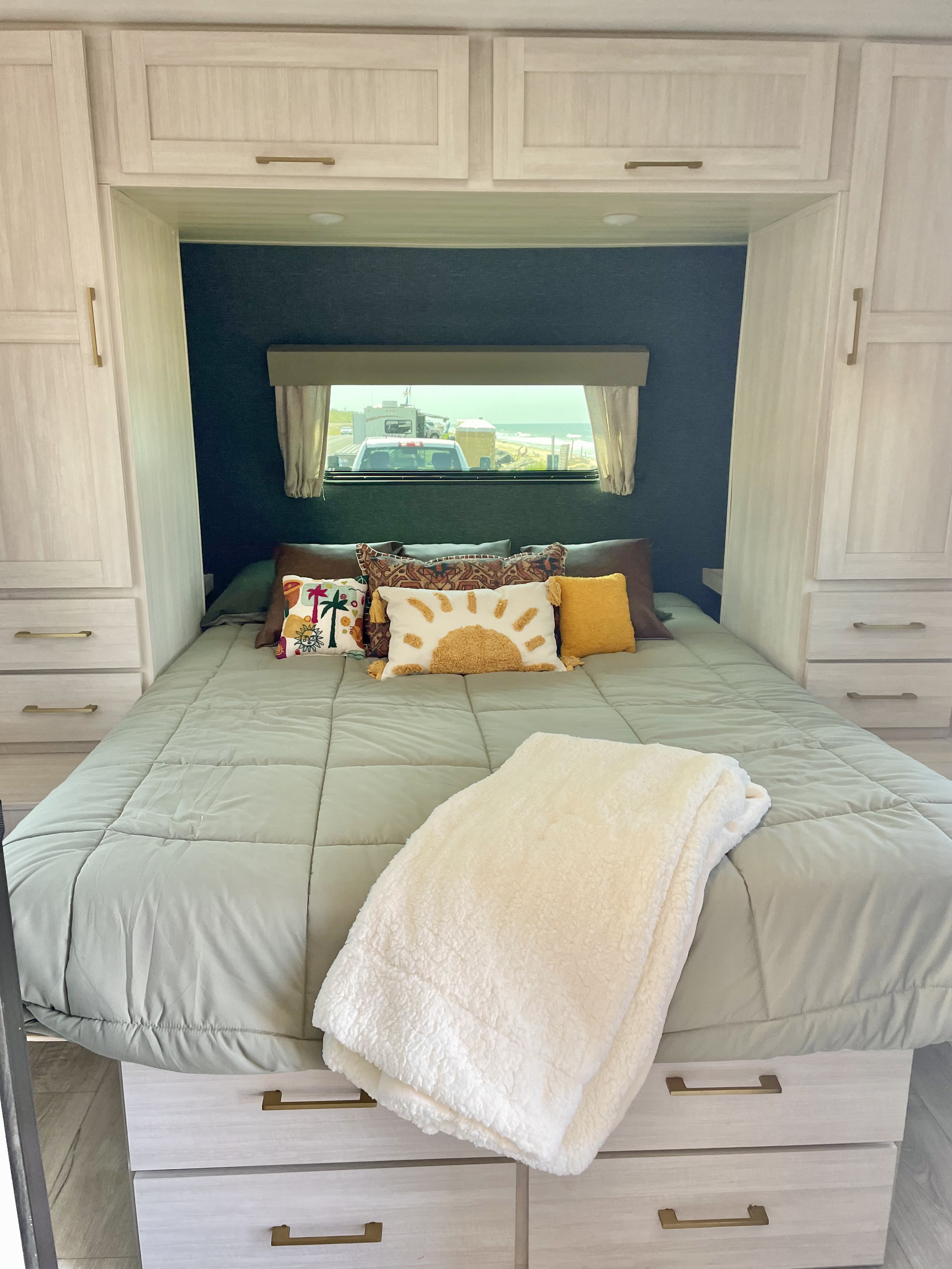 Modern RV rental bedroom featuring a cozy sage bed, soft blanket, decorative pillows, and ocean view.. Forest River Surveyor Legend 2024