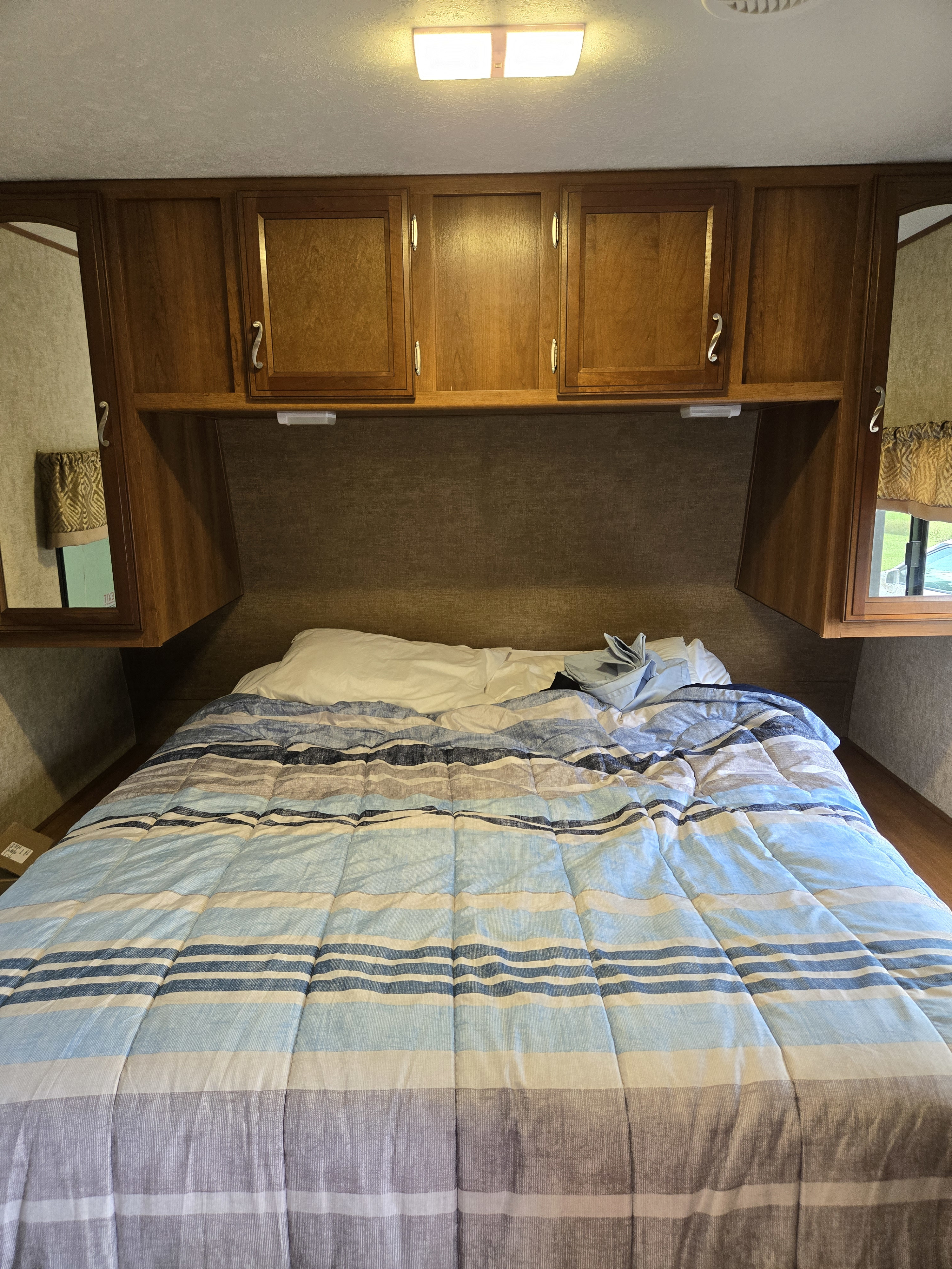 RV rental bedroom with a bed, blue and grey striped comforter, and wooden overhead cabinets. A cozy space for travel.. Avenger ATI 2017