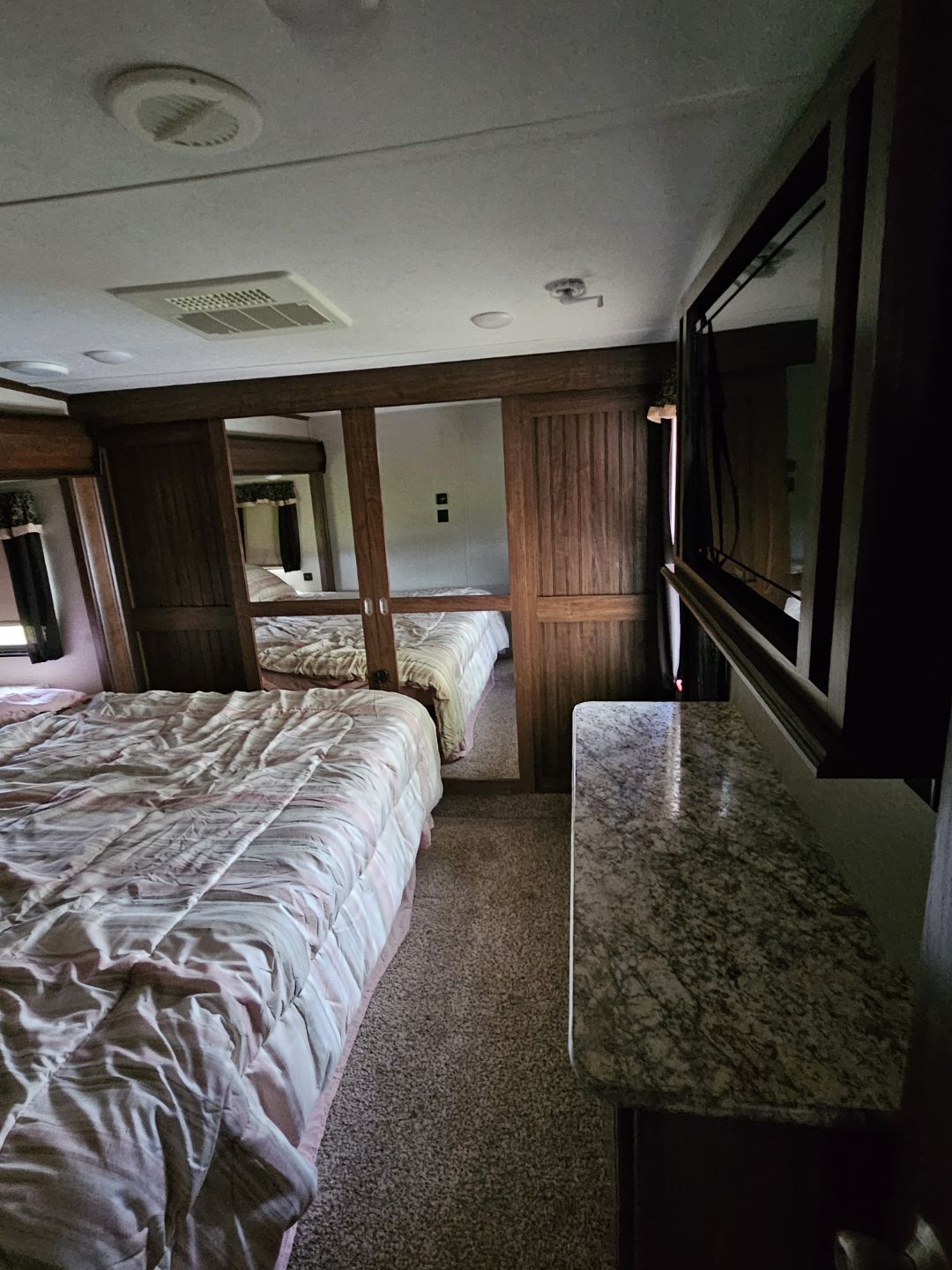 RV rental bedroom featuring a striped bed, mirrored closet, TV, and granite-like countertop. Cozy and functional interior.. Keystone RV Montana High Country 2017