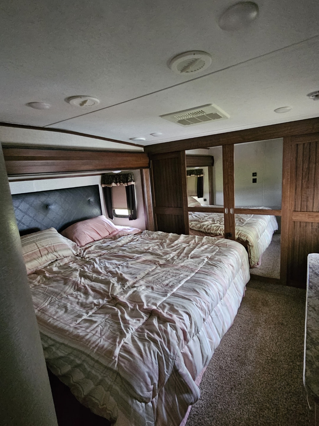Inside an RV rental: a cozy bedroom featuring a striped bed, mirrored wardrobe, and overhead vents. Ready for travel!. Keystone RV Montana High Country 2017