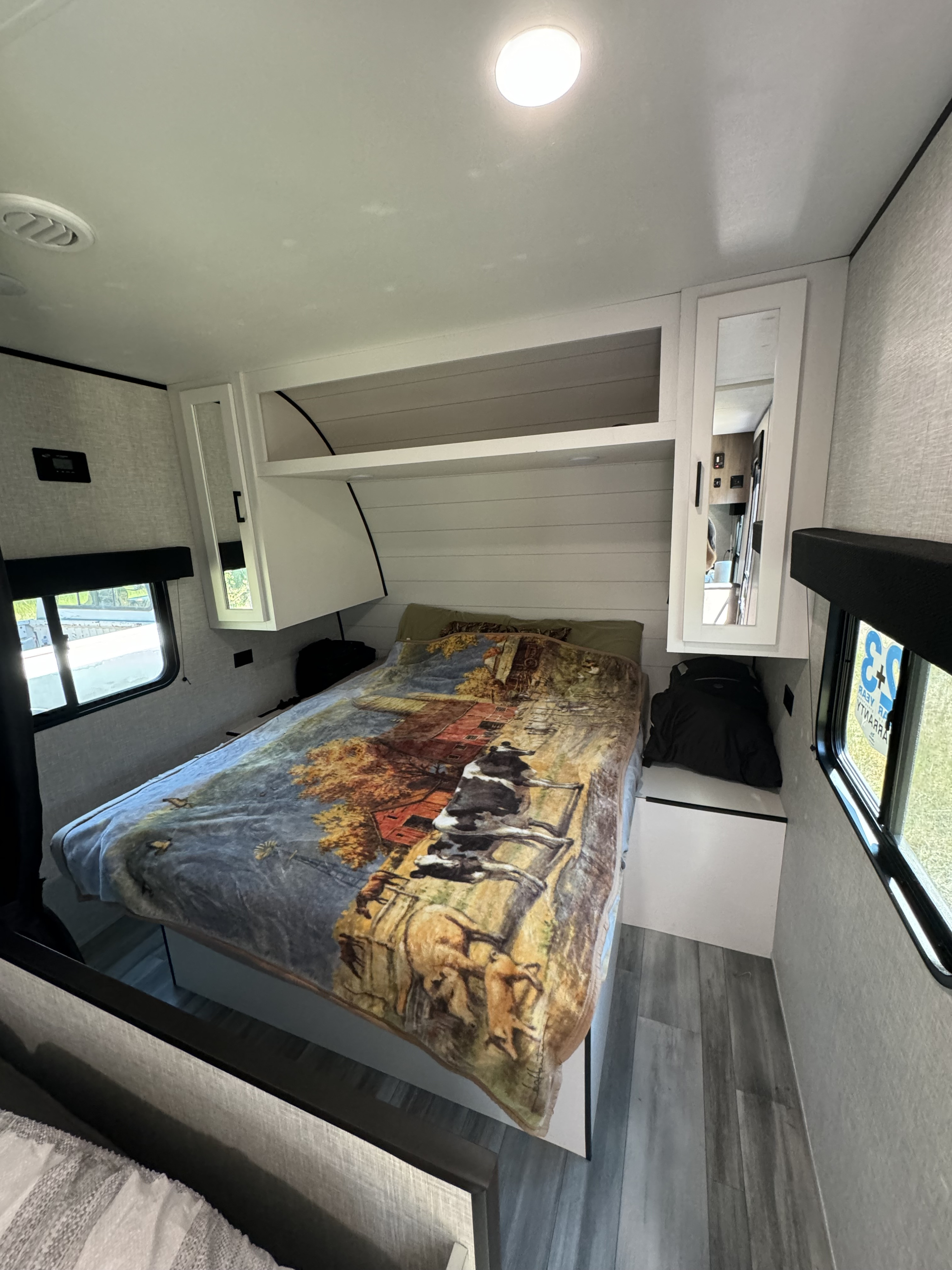 This RV rental features a cozy bedroom with a bed, unique farm-themed blanket, mirrored cabinet, and windows.. Jayco Jay Flight SLX 2024
