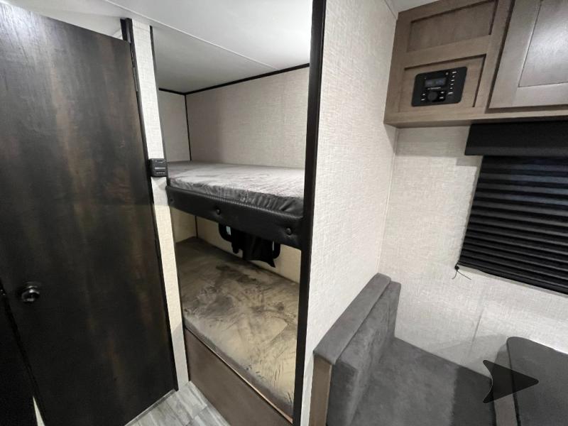 **RV rental interior** with bunk beds on the left, next to a dark wood door. A dinette with grey cushions is on the right.. Jayco Jay Flight SLX 2024