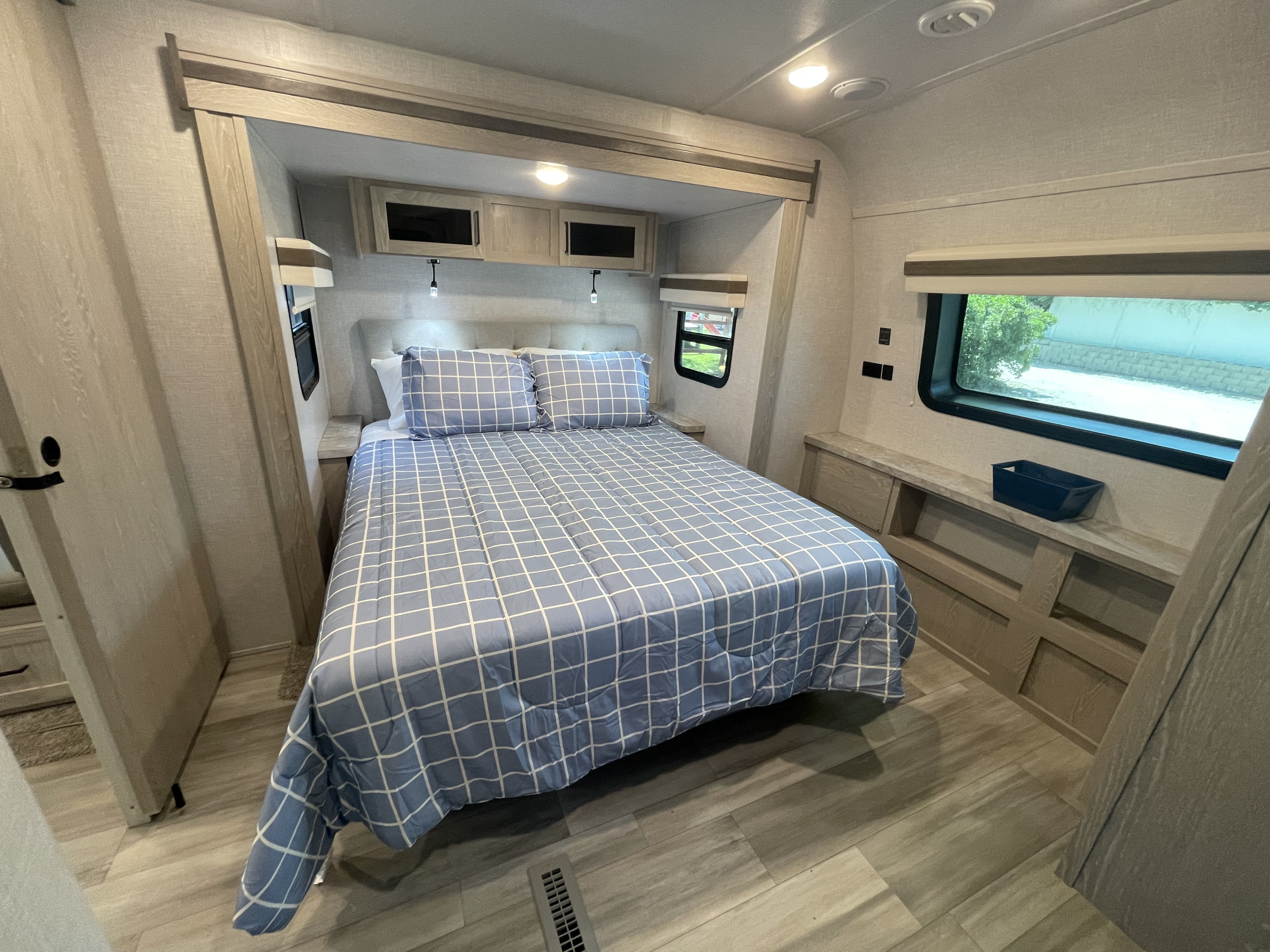 Cozy rv rental bedroom featuring a full bed with blue checkered bedding, light wood cabinetry, and small windows.. Forest River Rockwood Ultra Lite 2022
