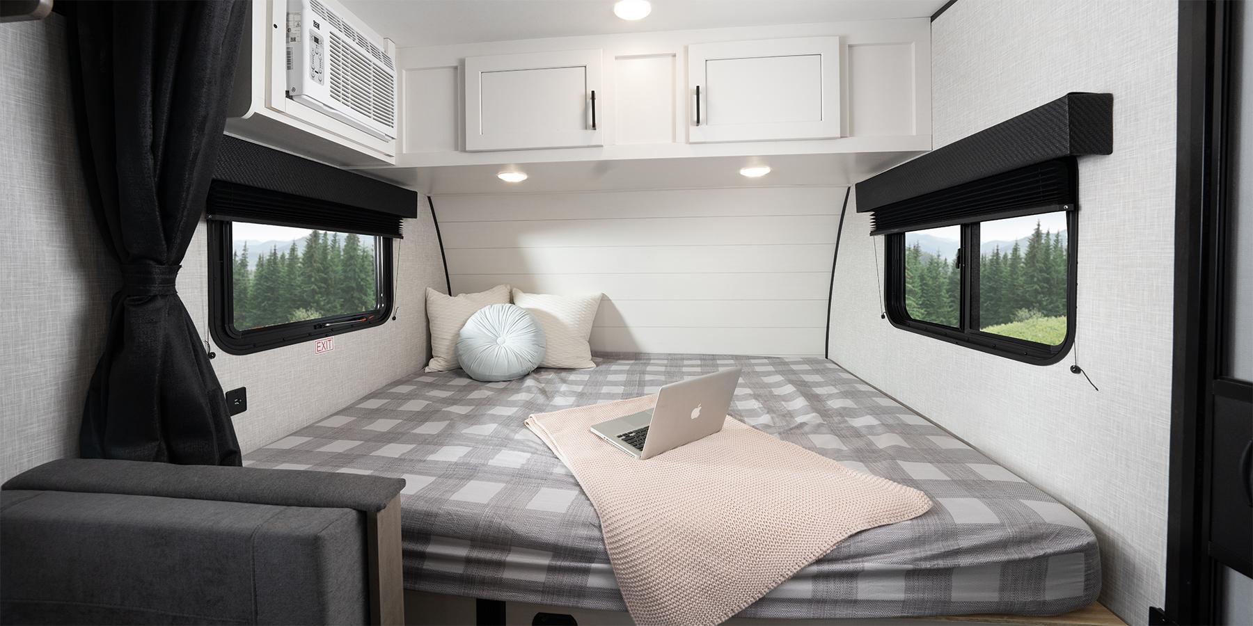 RV rental bedroom: cozy, compact space with plaid bed, laptop, AC, and large windows revealing a mountain view.. Jayco Jay Flight SLX 2024