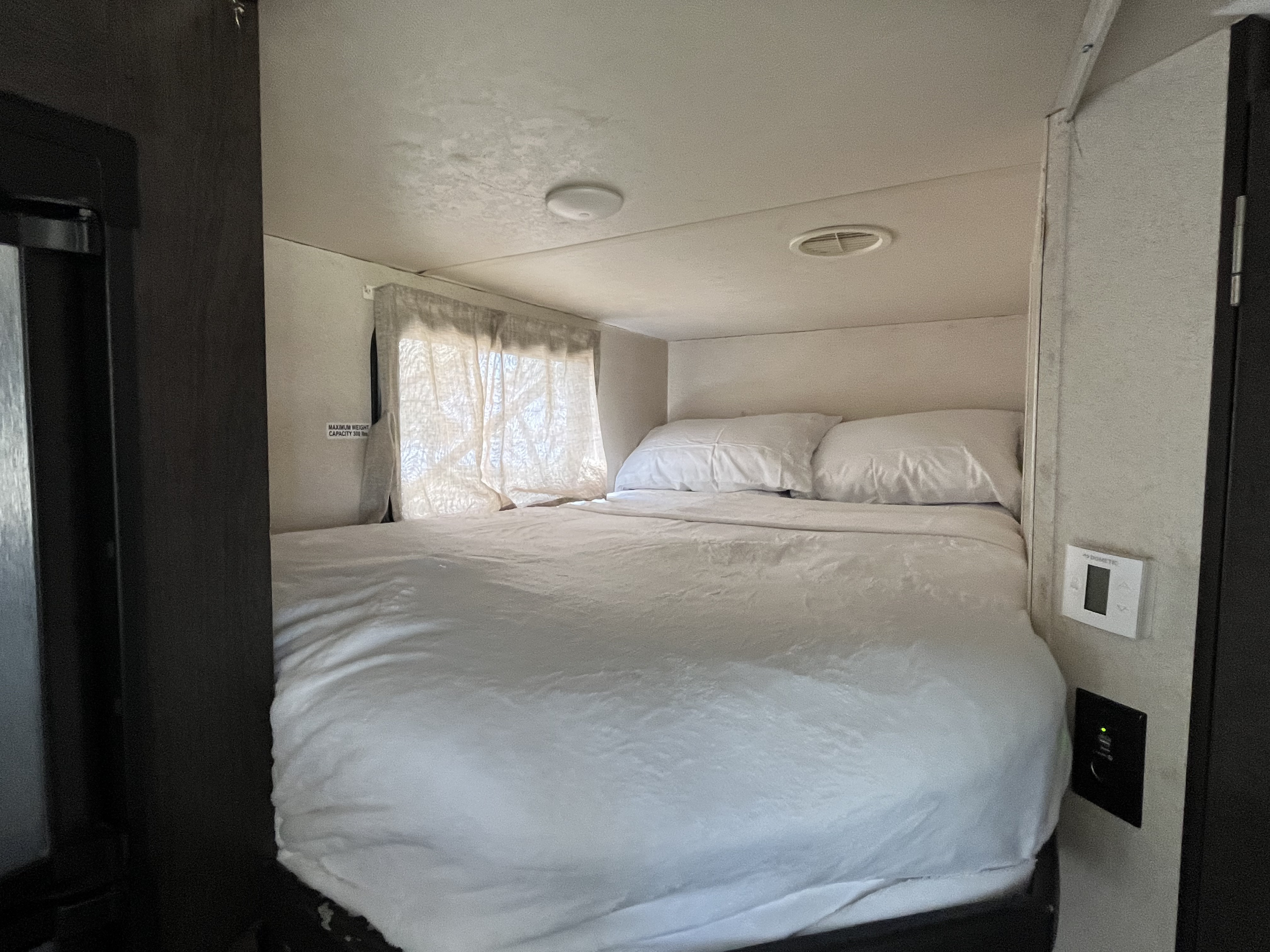 Compact RV rental bedroom with white bedding, window, climate control, and charging outlets. Max 350 lbs.. Forest River Wildwood X-Lite 2018