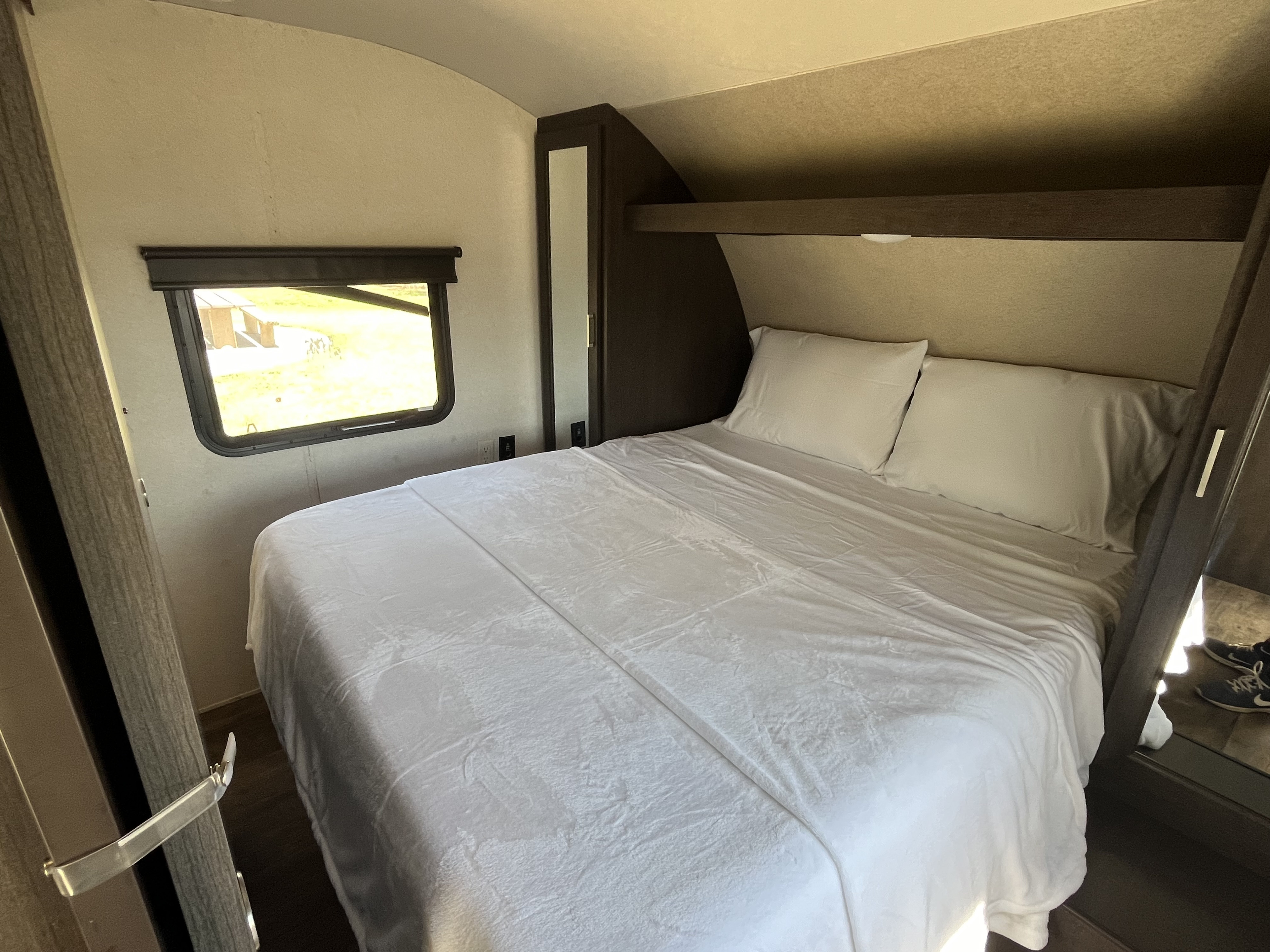 Cozy rv rental bedroom features a queen bed with white linens, a bright window view, and built-in cabinets.. Forest River Wildwood X-Lite 2018