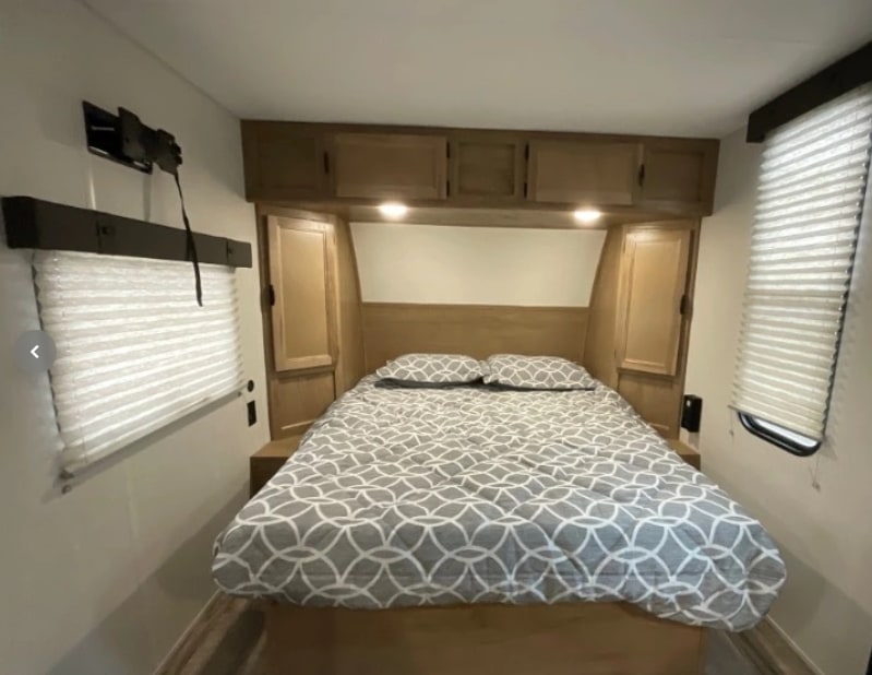 Cozy RV rental bedroom: patterned bed, overhead storage, window blinds, and a TV mount ready for entertainment.. Forest River Cherokee Wolf Pup 16KHWBL 2024