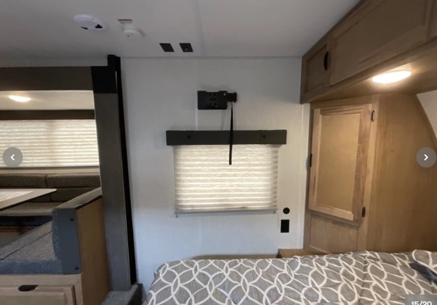 RV rental interior: cozy bedroom with patterned bedding, window with blinds, TV mount, and a dinette area on the left.. Forest River Cherokee Wolf Pup 16KHWBL 2024