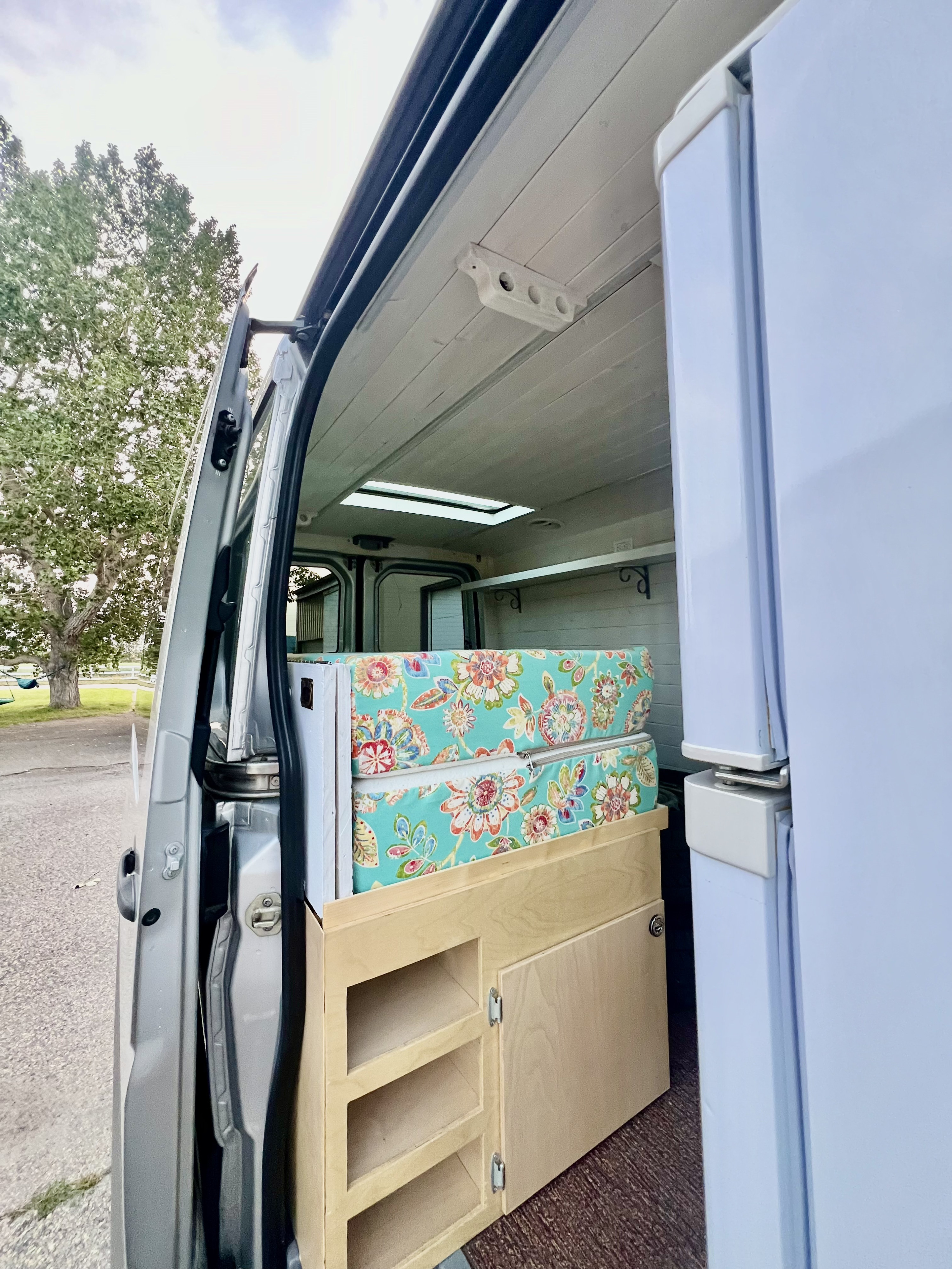 Explore this cozy rv rental! Custom camper van interior with floral cushions, wood cabinets, and fridge.. Mercedes Sprinter 2016