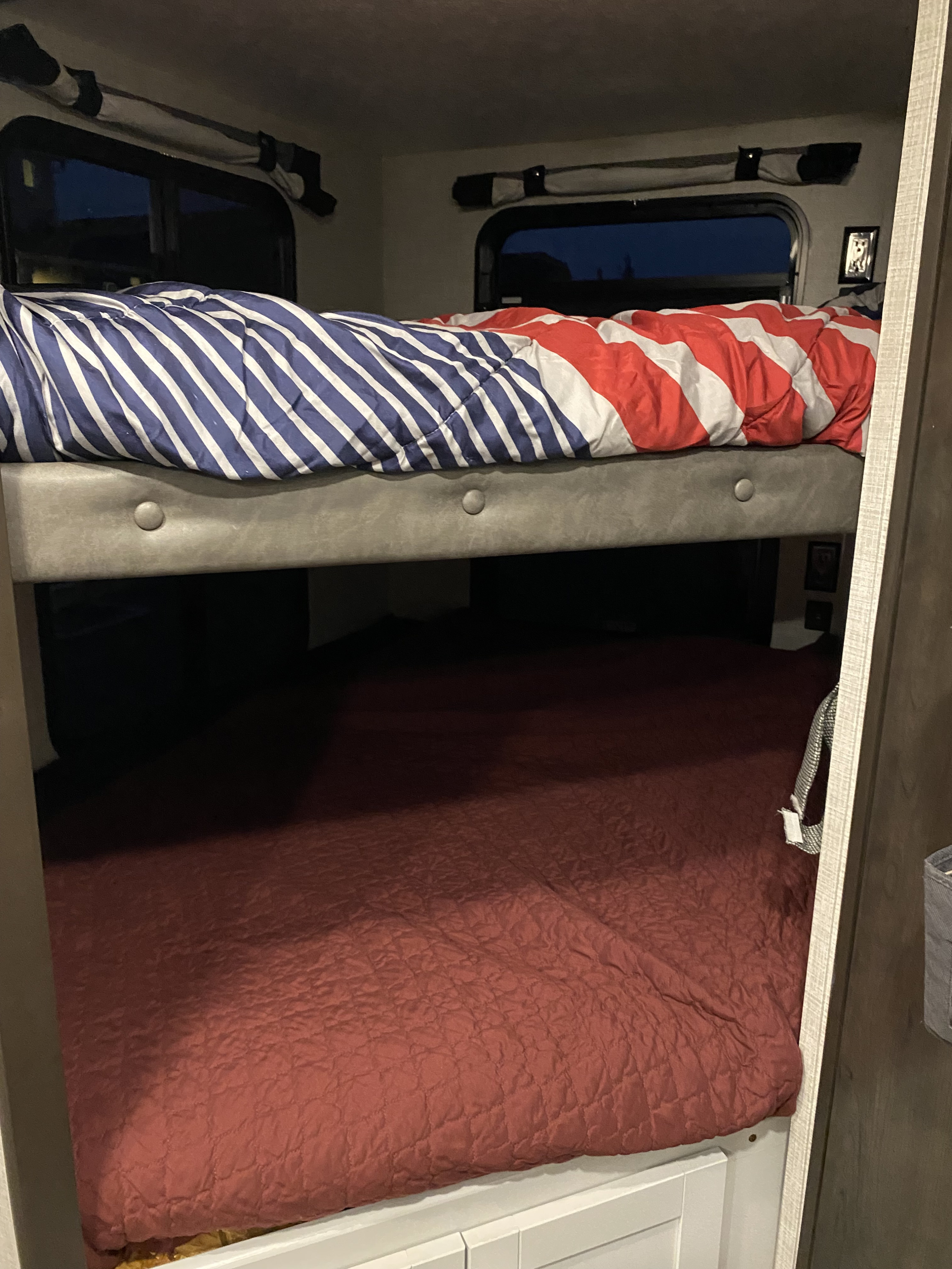 Relax in this rv rental's cozy bunk beds. Upper features striped bedding, lower has a quilted red comforter.. Keystone Bullet 2021