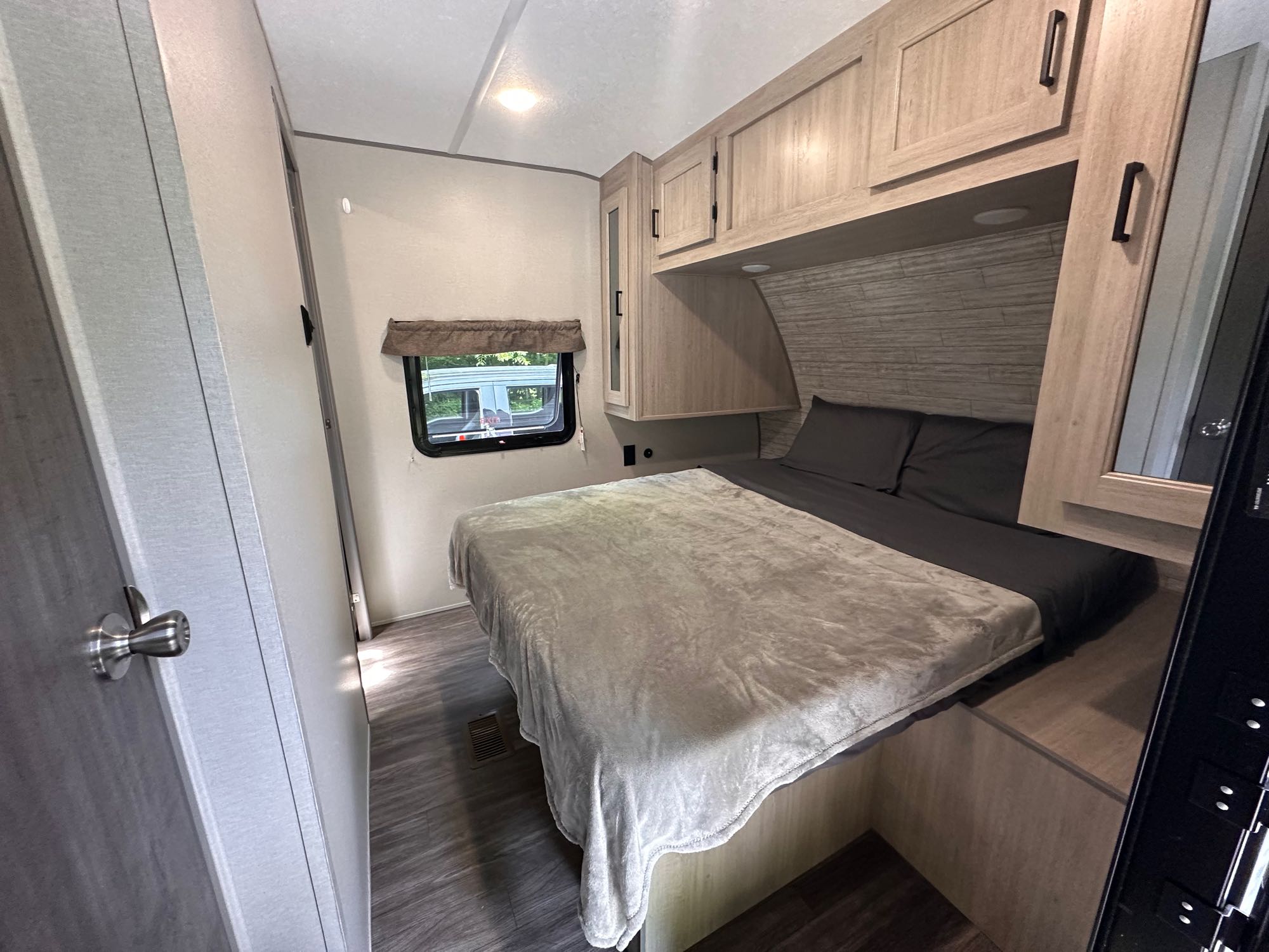 Cozy RV rental bedroom with a comfortable bed, overhead cabinets, and a window providing natural light. Perfect for travel.. Forest River Aurora 28BHS 2024