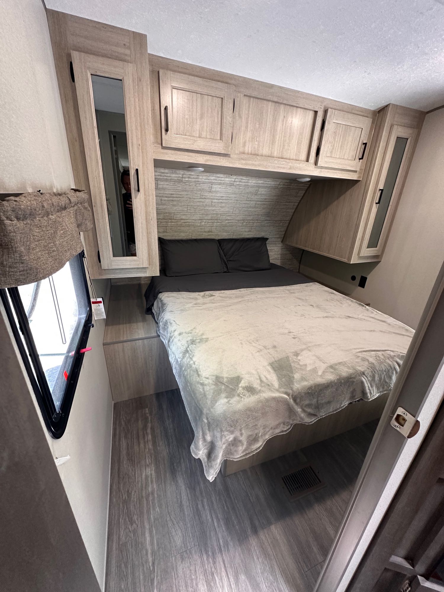 This inviting rv rental bedroom features modern light wood-look cabinetry, a bed with grey bedding, and a mirrored wardrobe.. Forest River Aurora 28BHS 2024