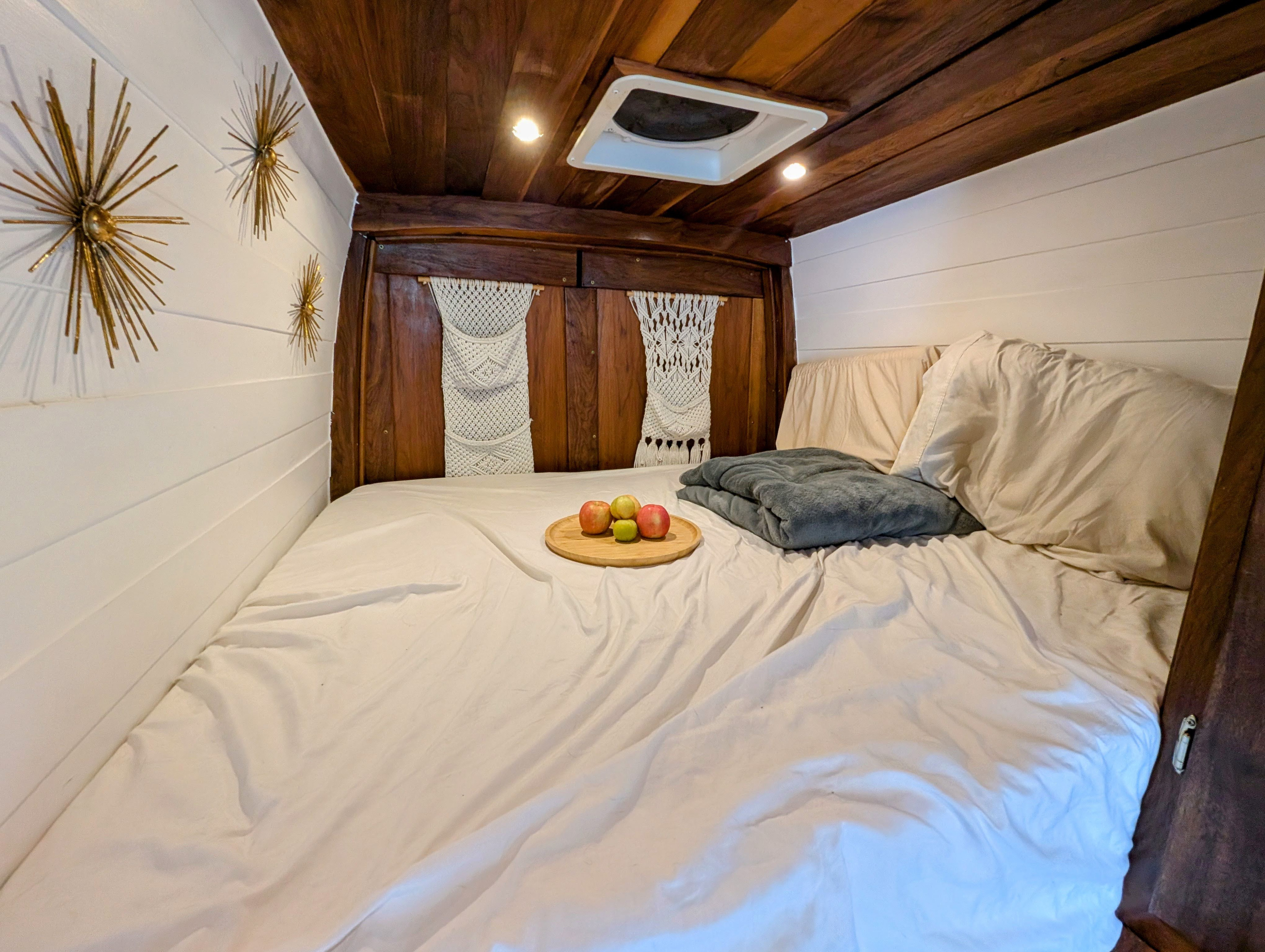 Cozy RV rental bedroom with a large bed, warm wood and white paneling, and unique starburst wall decor. Apples on tray.. Mercedes-Benz Sprinter 2018