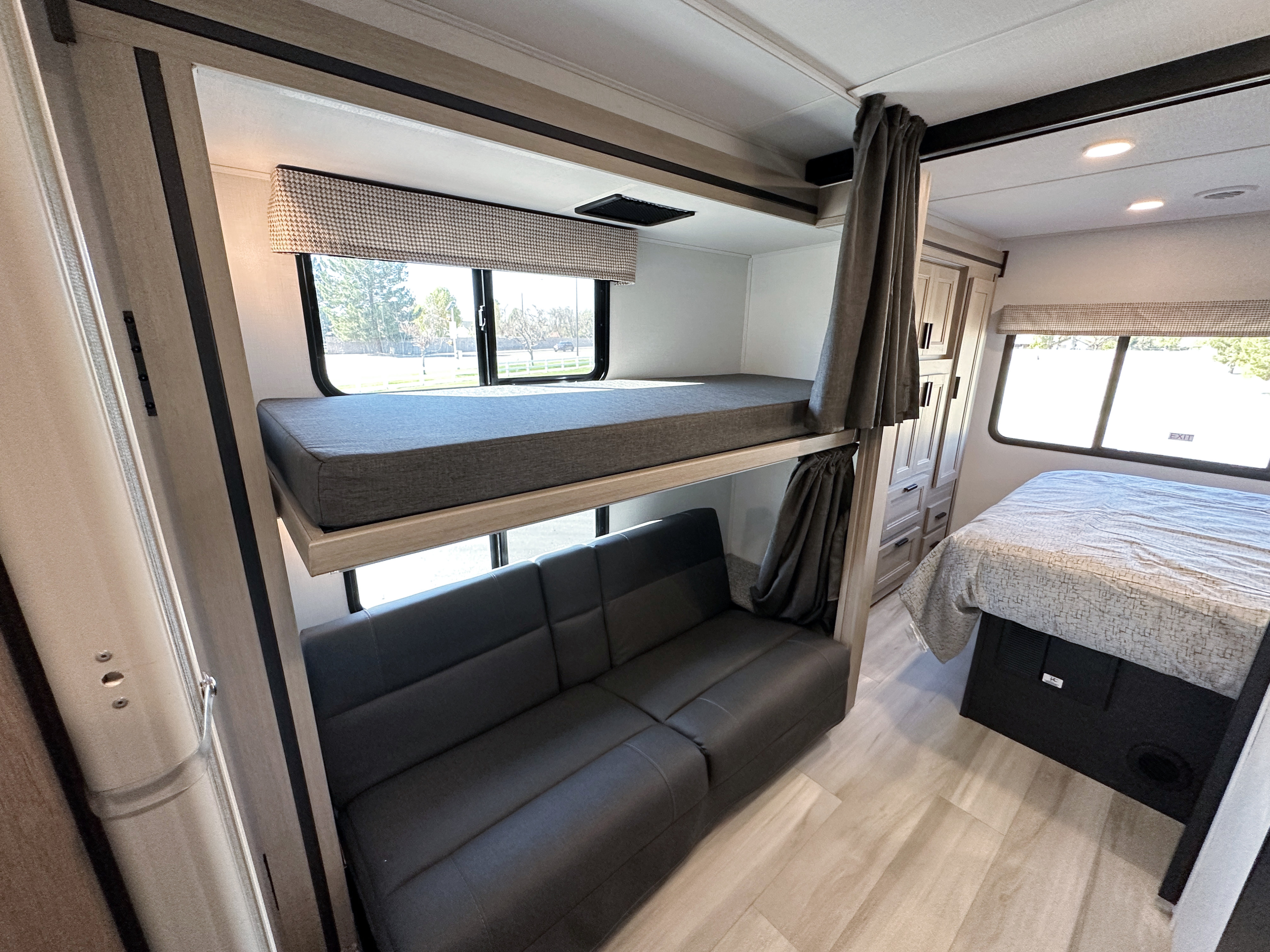 Inside an RV rental: bunk beds with a sofa, a main bed, and light wood flooring. A compact, family-friendly mobile living space.. Forest River Sunseeker 2024