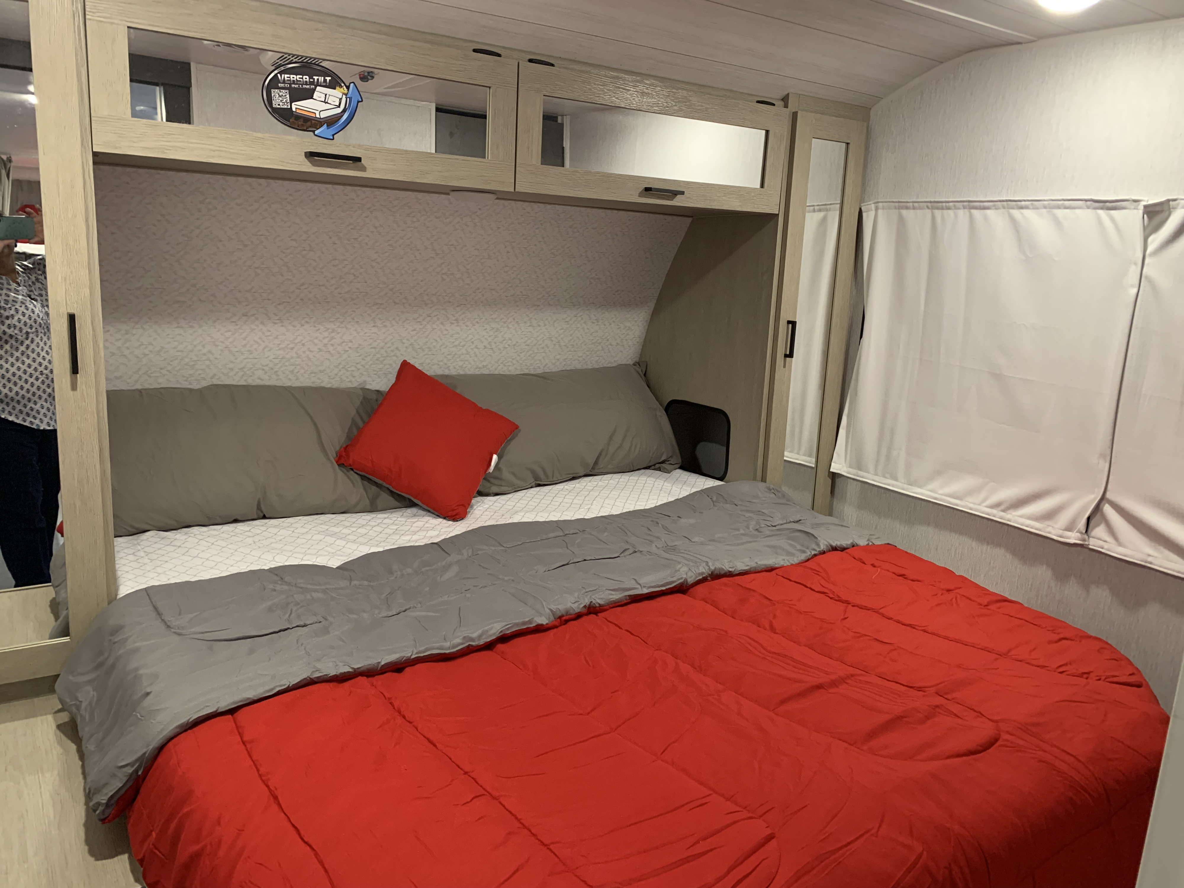 Relax in this RV rental bedroom featuring a comfortable bed with red comforter, grey pillows, and Versa-Tilt bed incliner.. Forest River Wildwood Platinum 2024