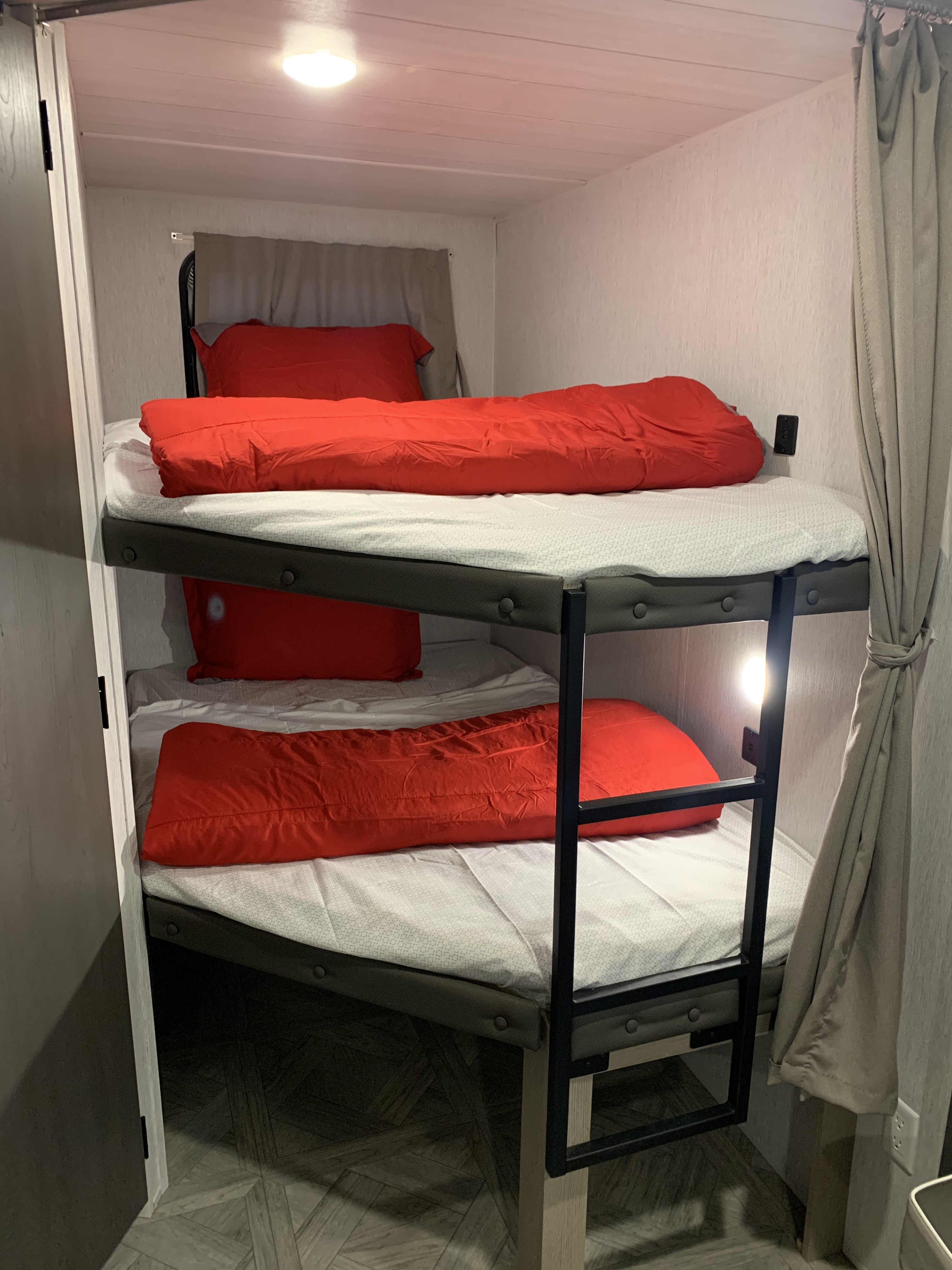 RV rental interior: two stacked bunk beds with bright red bedding, offering compact sleeping & a reading light.. Forest River Wildwood Platinum 2024