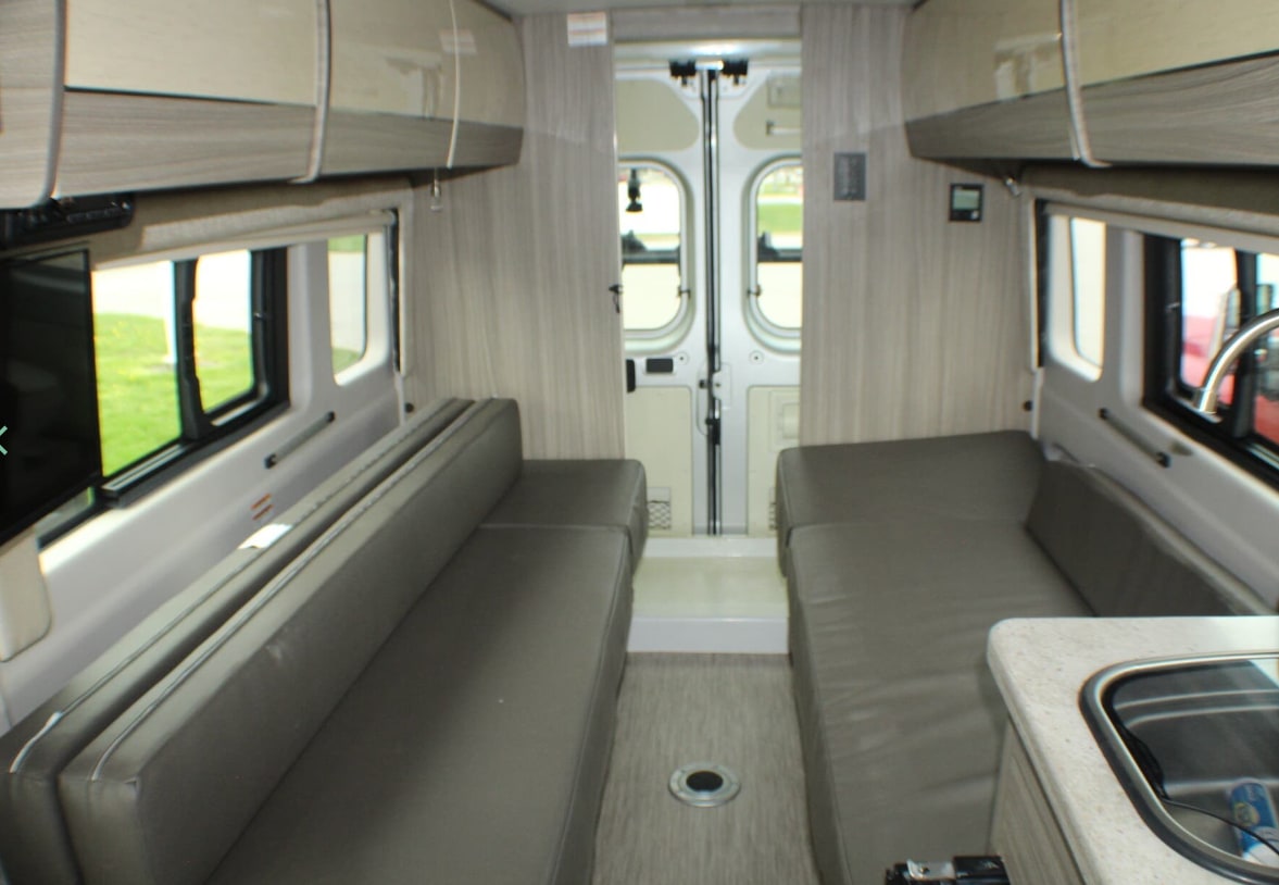 Interior of an RV rental: cozy camper van with two bench seats, overhead storage, and a compact kitchen.. Jayco Swift 2022