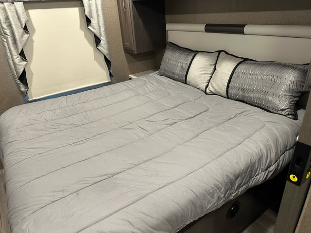 Inside a comfortable RV rental bedroom, showing a made bed with gray comforter and decorative pillows.. Thor Miramar 2022