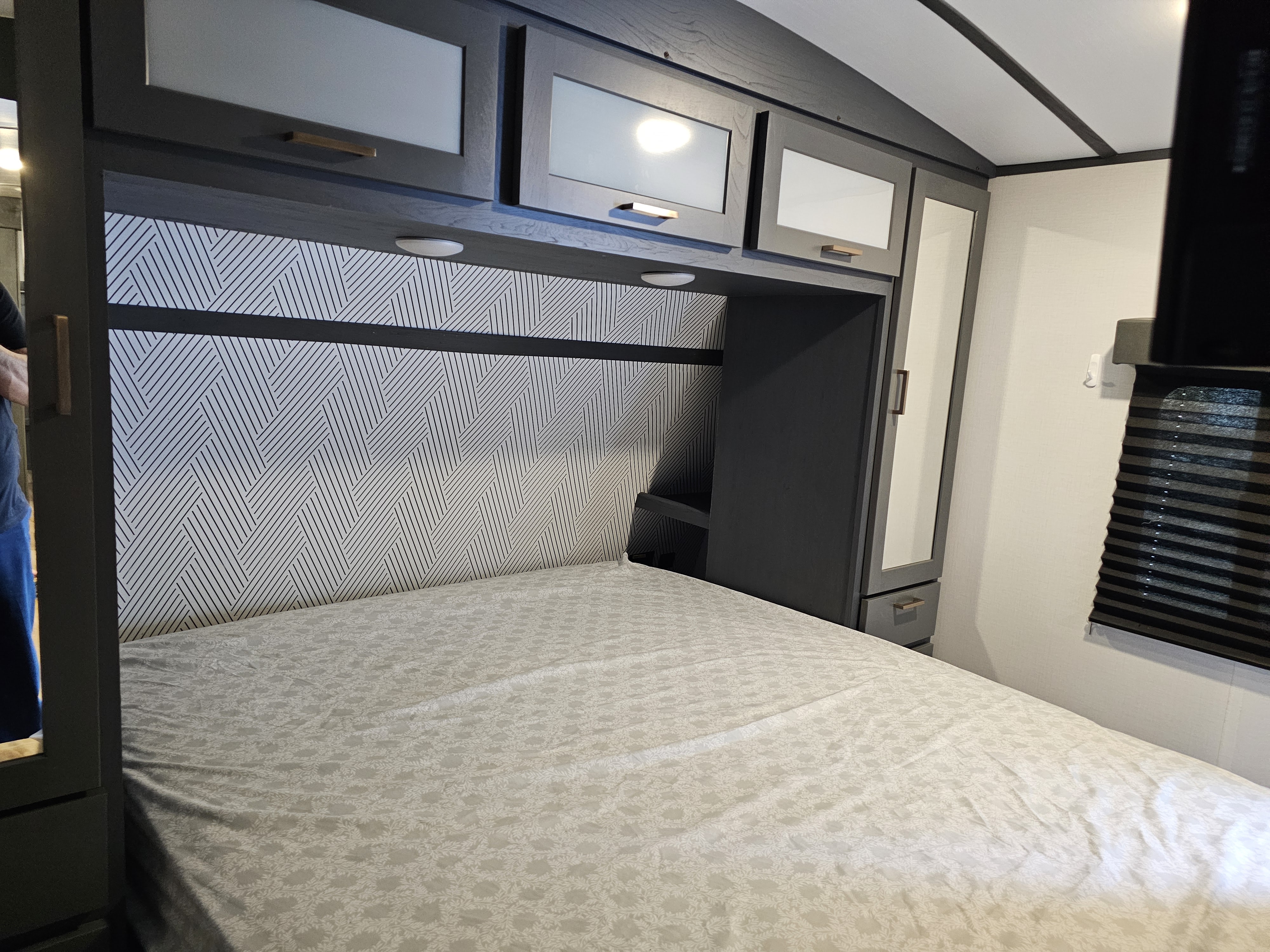 Cozy RV rental bedroom featuring a bed, patterned headboard, and overhead storage cabinets for a comfortable stay.. Keystone RV Bullet Ultra Lite 2023