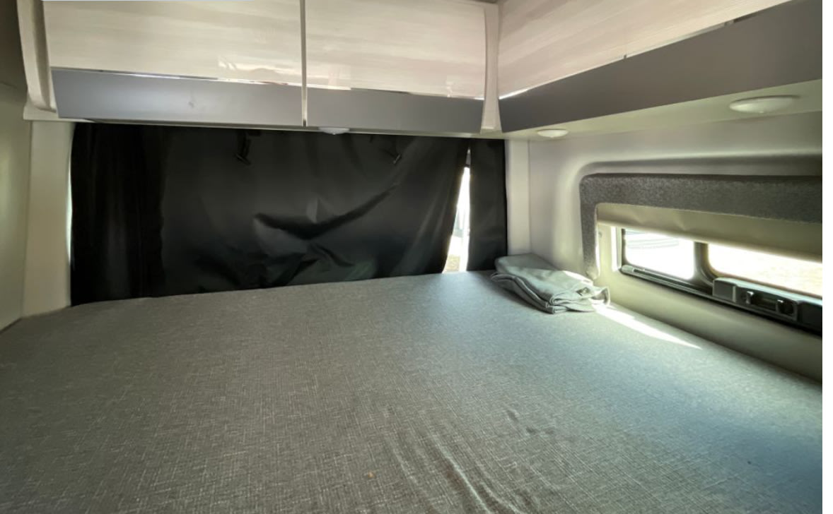 Cozy RV rental bedroom with blackout curtains, gray bed, and overhead storage for comfortable travel.. Thor Sanctuary 2024