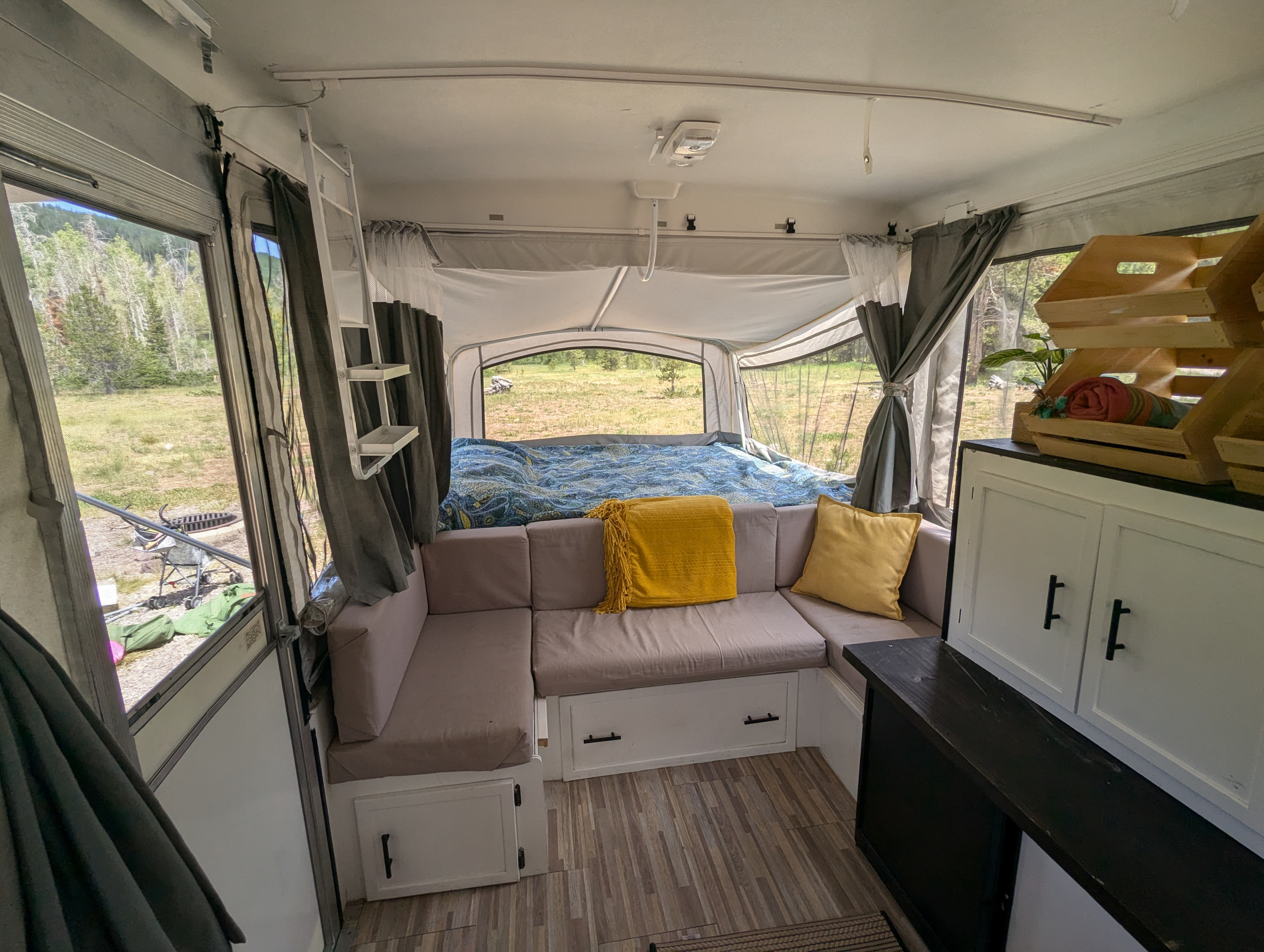 Inside a pop-up RV rental, featuring an L-shaped couch, bed, and outdoor views through screened windows.. Coleman Grand Tour Mesa 1999