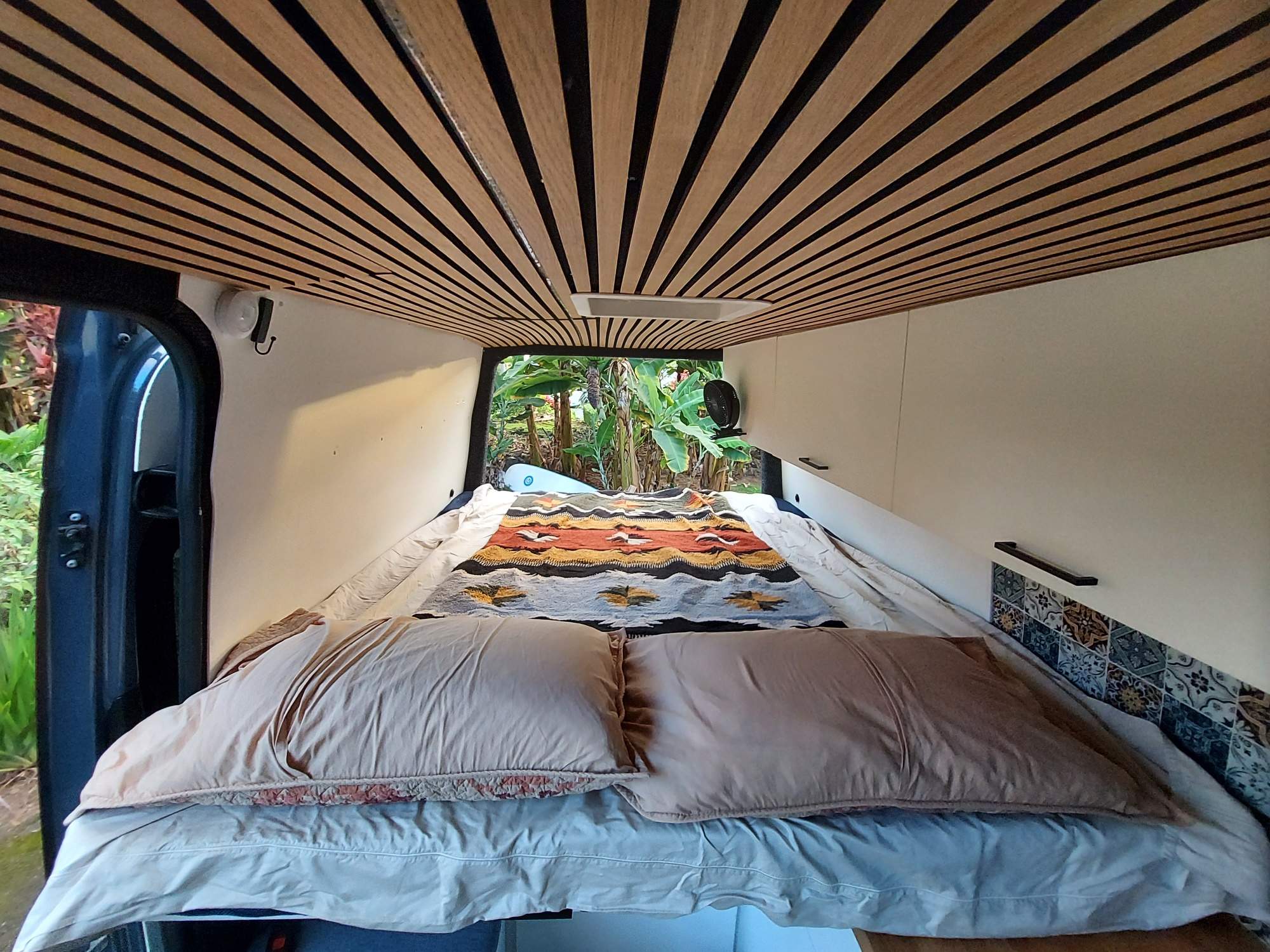 Comfortable camper van interior for your next rv rental adventure. Features a cozy bed, unique slatted ceiling & lush nature view.. Mercedes-Benz Sprinter 2018