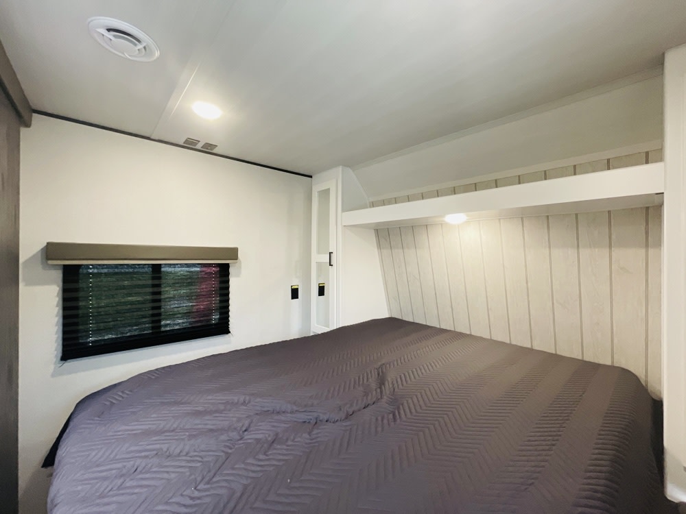 Experience comfort in this RV rental bedroom. Features include a full bed, window with blinds, and integrated storage.. Keystone RV Hideout 2023