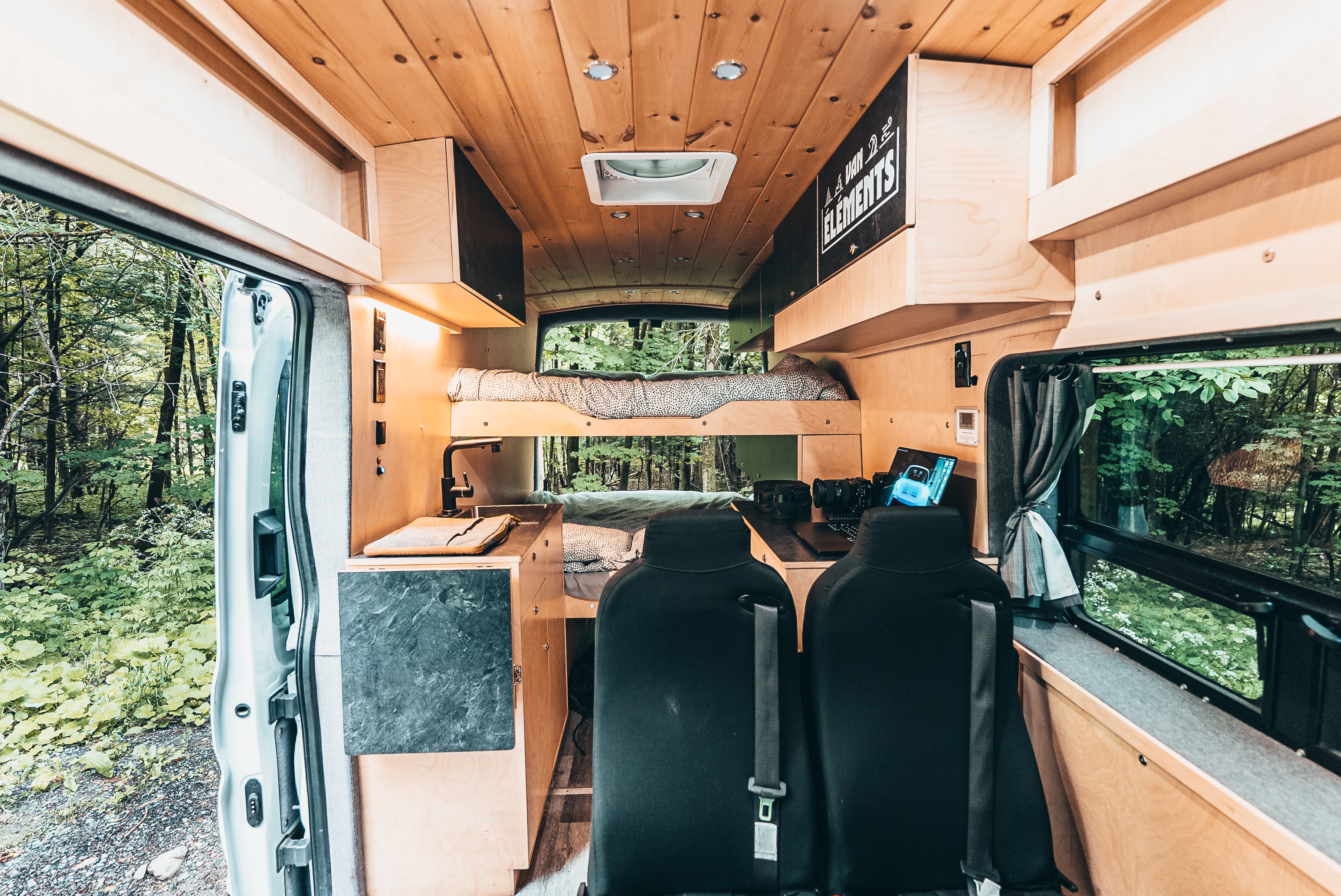 Spacious RV rental interior with bunk beds, kitchenette, and forest views.. Ford Van 2023