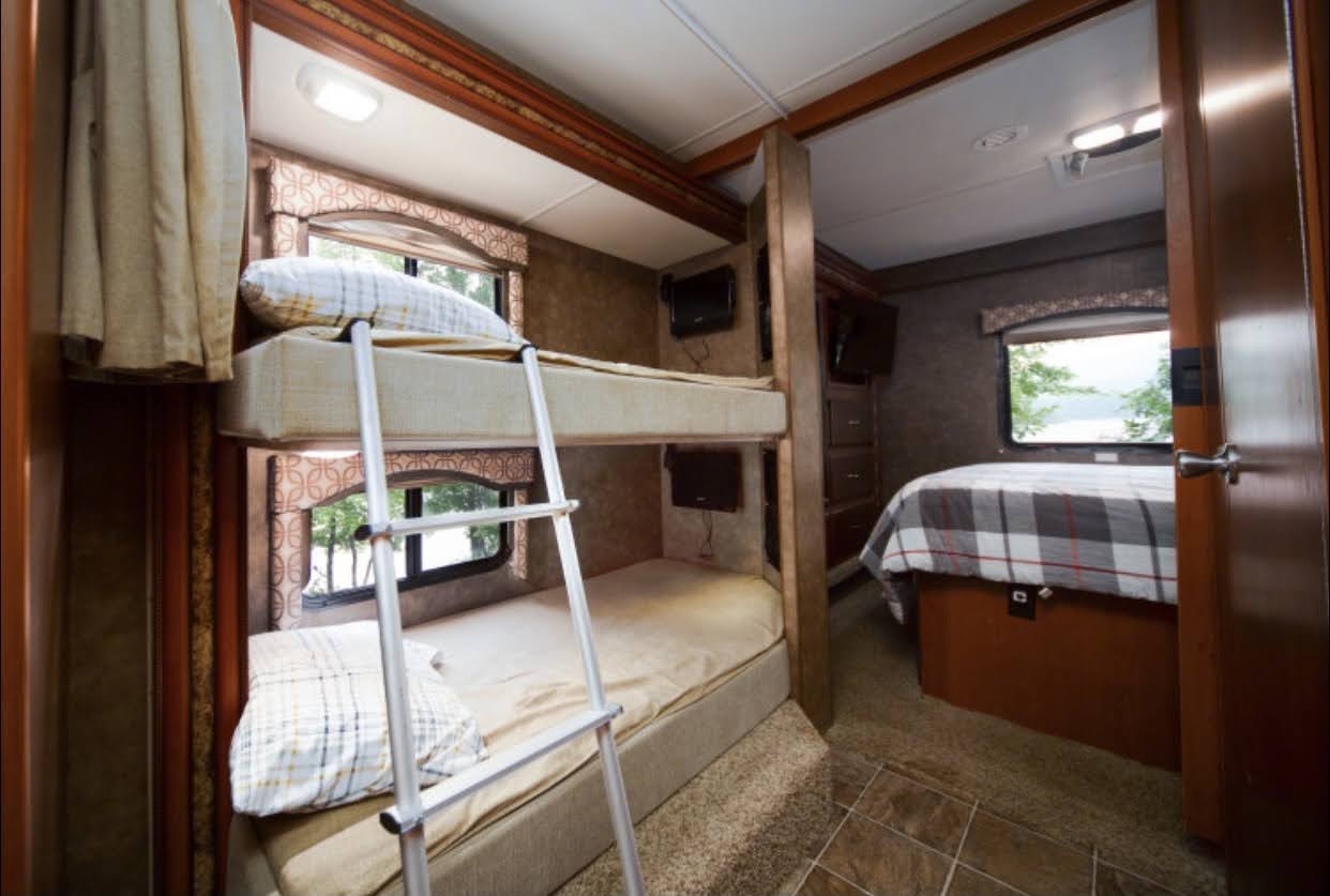 Spacious RV rental interior featuring bunk beds with ladder, individual TVs, and a private bedroom with scenic window views.. Other Four Winds 2013