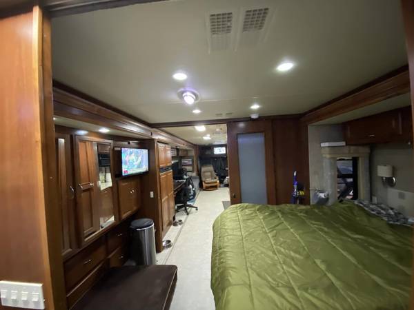 Inside a comfortable RV rental: Master bedroom with green comforter, TV, and detailed wooden cabinetry in a spacious motorhome.. Fleetwood Southwind 35D 2008