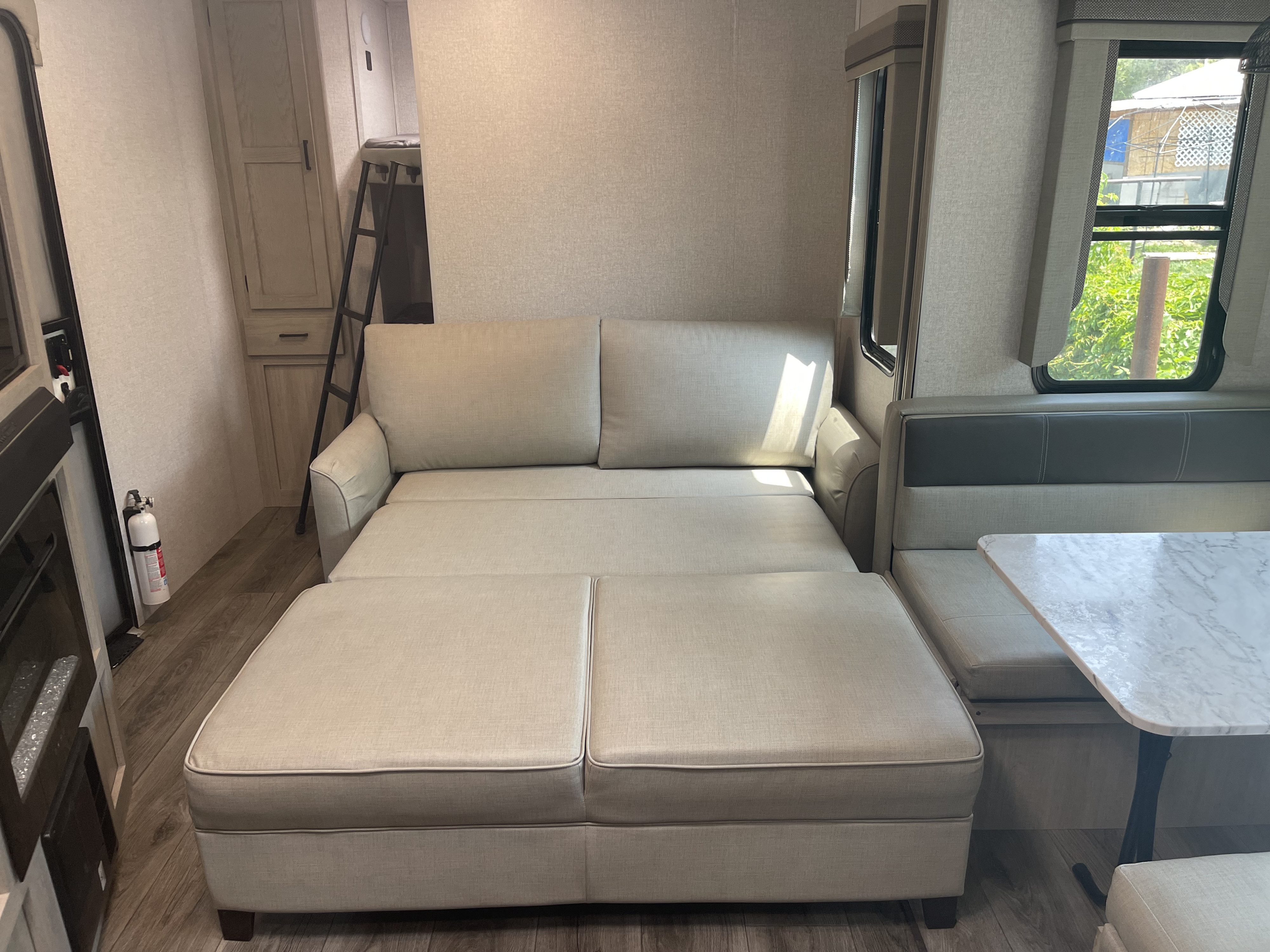 Inside an RV rental: sofa converts to a pull-out bed, with a dining booth and bunk beds. Modern interior.. East to West Alta 2022