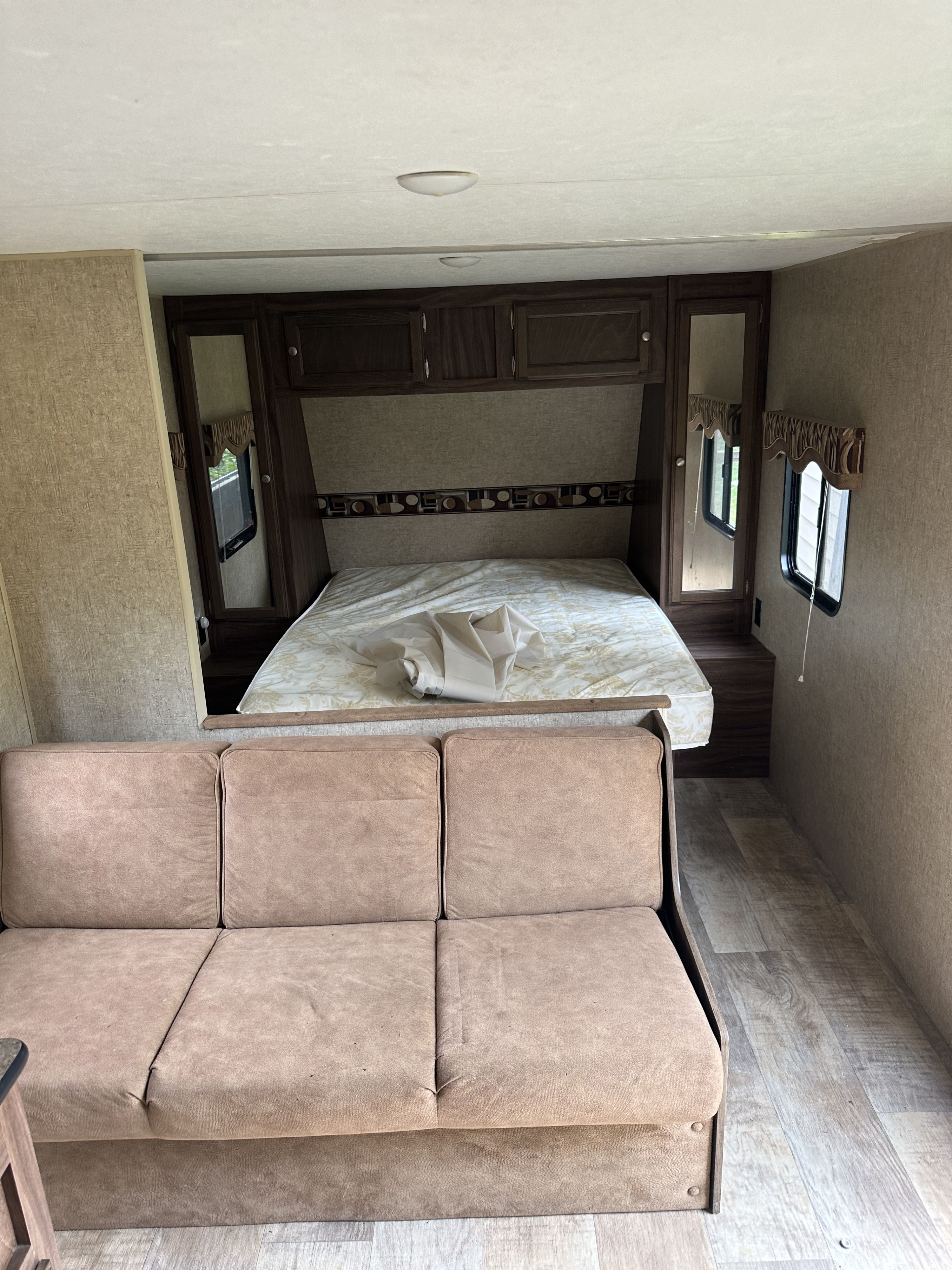 Spacious RV rental interior featuring a bedroom with a bed & cabinets, plus a brown sofa in the living area.. K-Z Manufacturing Sportsmen 2016