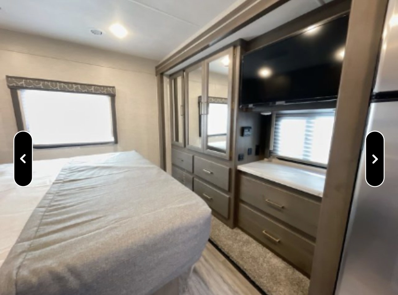 Spacious RV rental bedroom showcasing a comfortable bed, built-in dresser, mirrored wardrobe, and mounted TV. Ideal for travel comfort.. Thor Resonate 2024