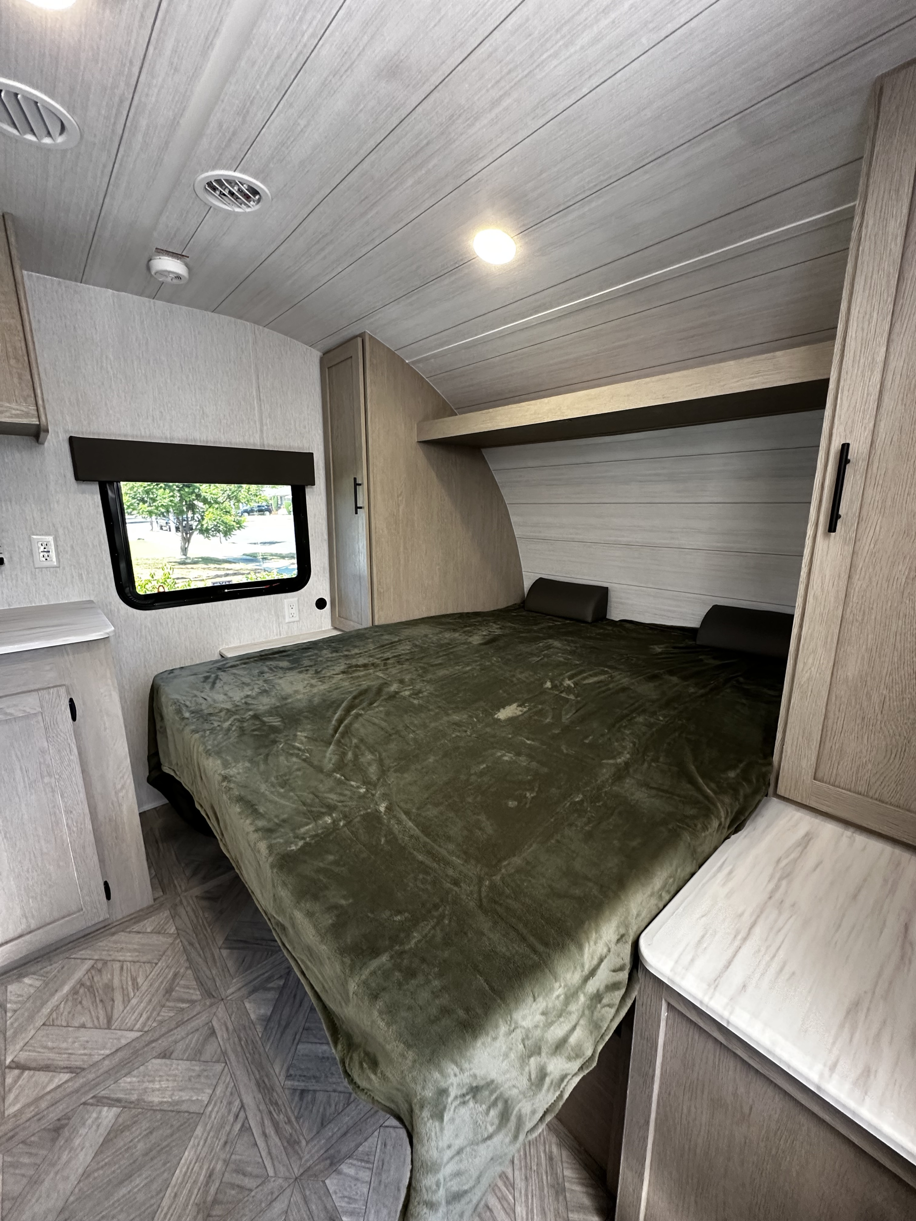 Inside a modern RV rental bedroom featuring a comfy bed, window view of trees, and light wood cabinetry.. Forest River EVO 2024