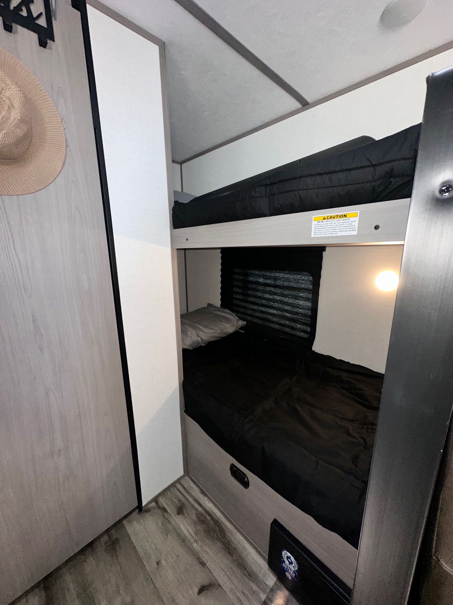 RV rental interior: cozy bunk beds with black bedding, a window, and a light. Comfortable sleeping area in a camper.. Dutchmen Coleman 17B 2024