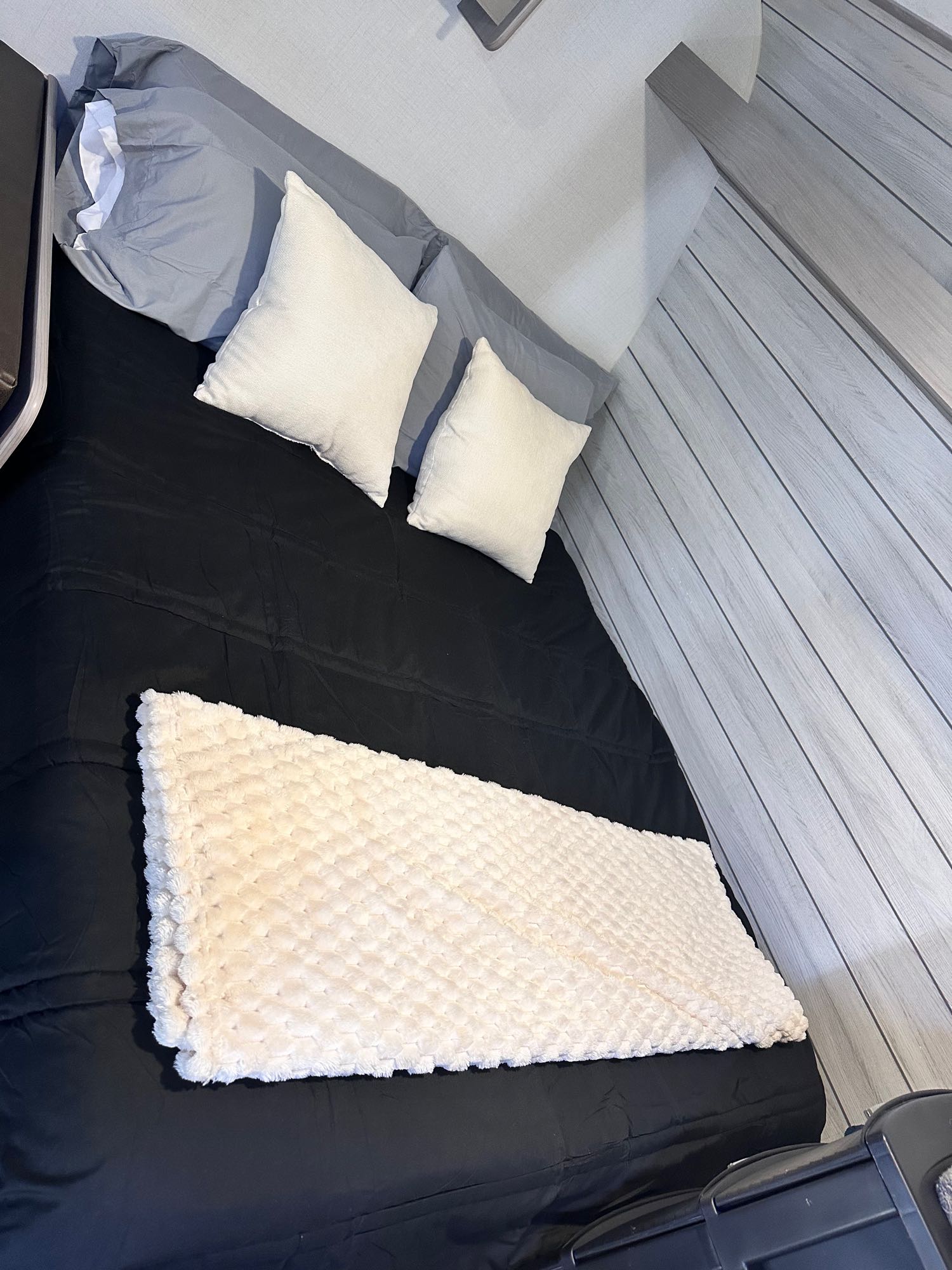 RV rental's compact bedroom: black bed, white pillows, soft cream blanket, and light paneled walls for cozy travel.. Dutchmen Coleman 17B 2024