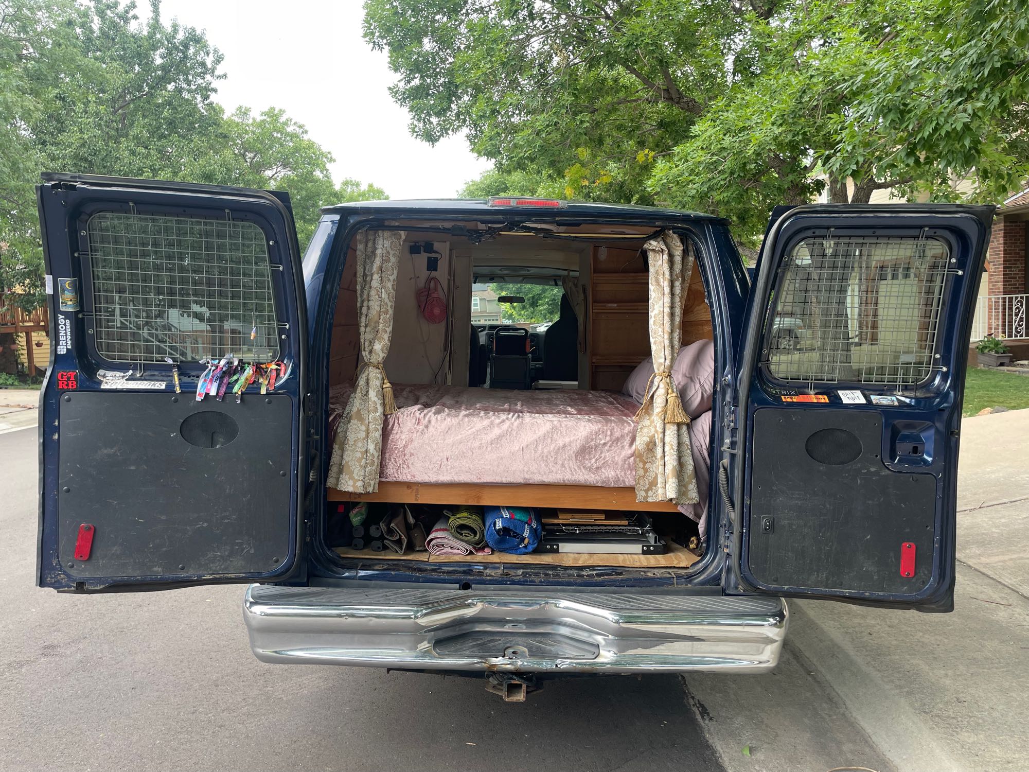 A custom blue camper van with open rear doors revealing a bed and organized storage inside, ready for RV rental adventures.. Ford Econoline 2010