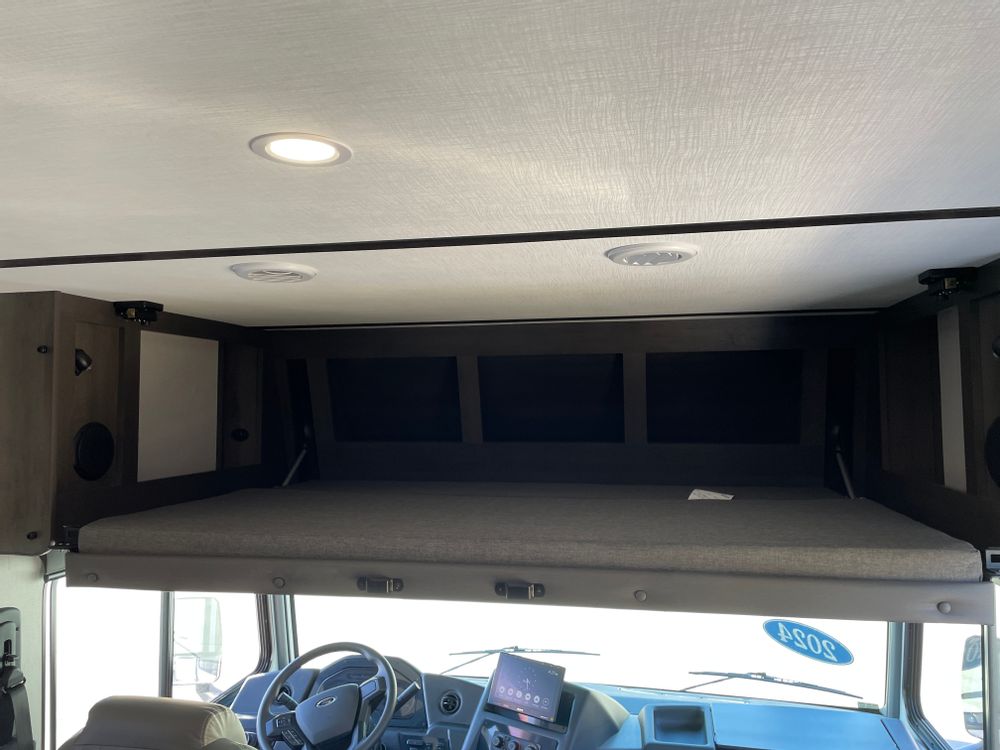 Interior of an RV rental showing the cab-over bunk bed, storage compartments, and the vehicle's dashboard below.. FR3 FR3 Motorhome 2024