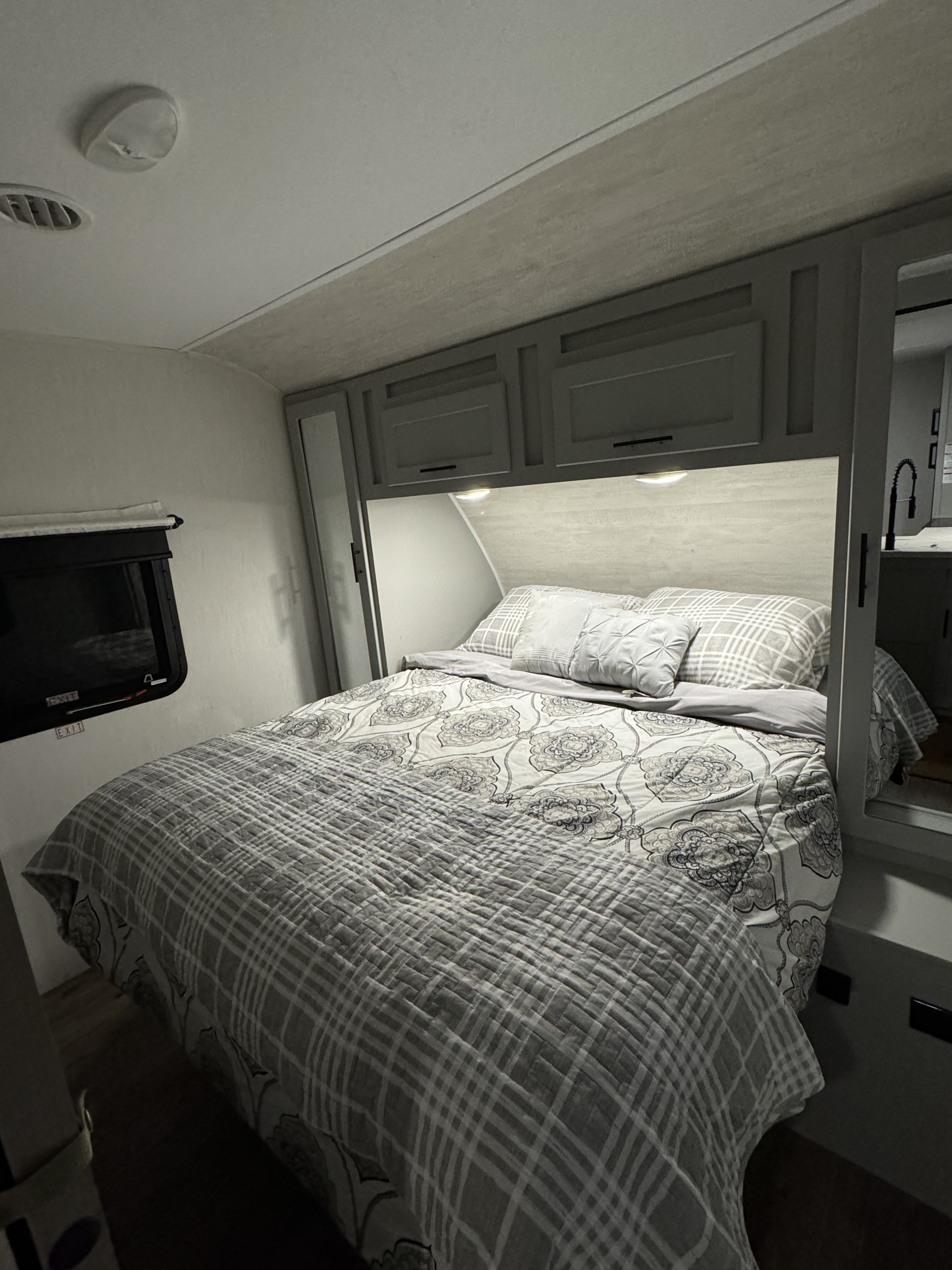 Cozy RV rental bedroom with a patterned bed, practical overhead cabinets, and a window with an exit label.. Forest River Vibe 2021