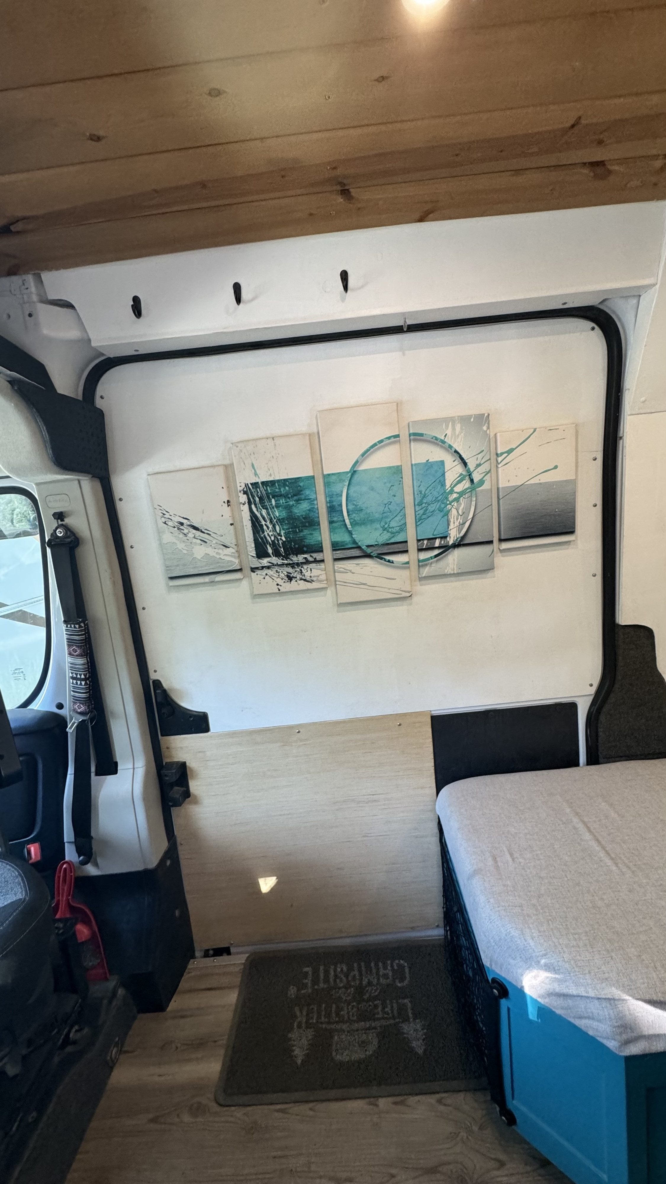 Cozy rv rental interior featuring wood paneling, abstract art, a comfy bed, and a "Campsite" mat.. Dodge B Van 2021