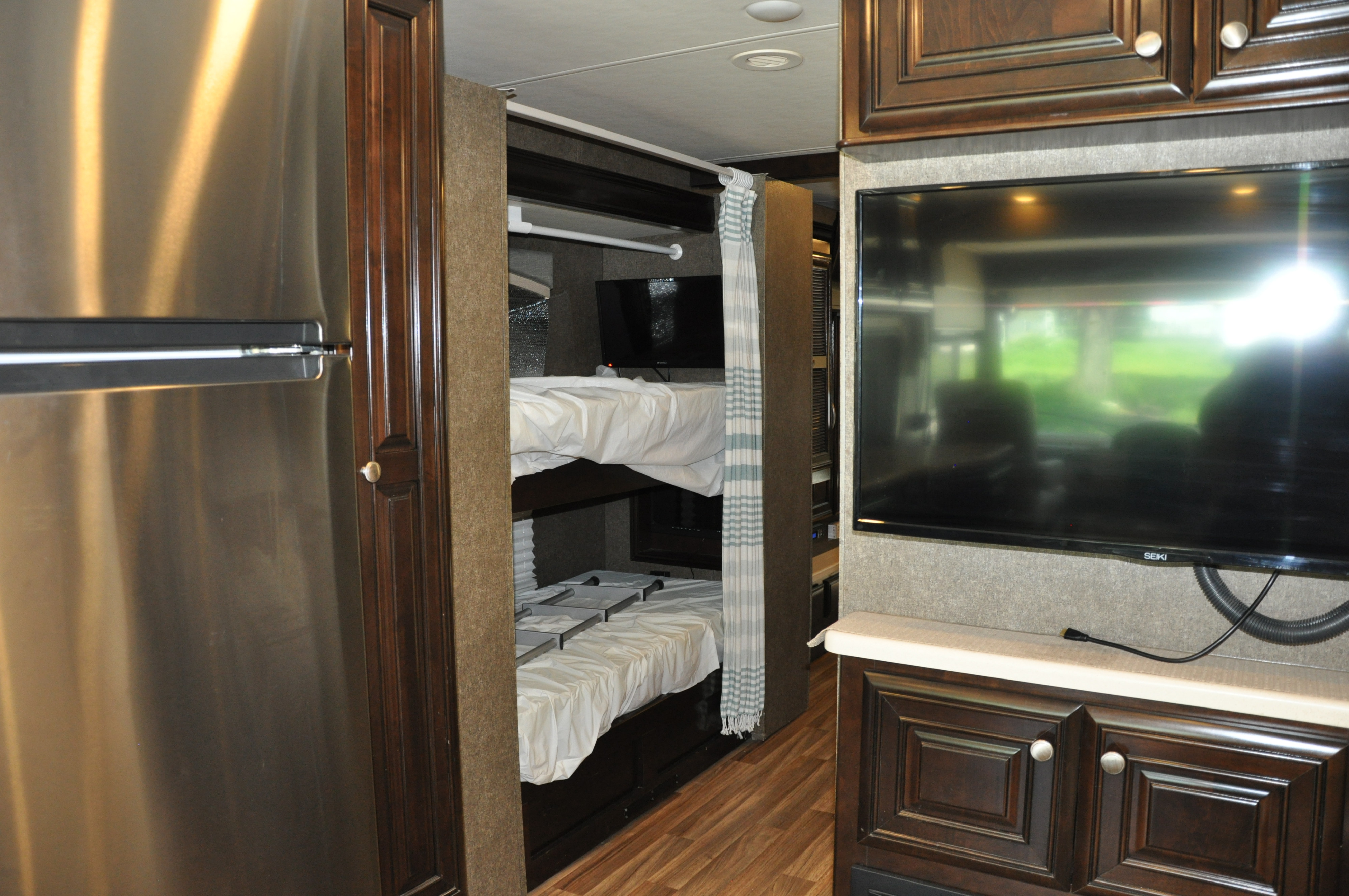 RV rental interior featuring a stainless steel fridge, wooden cabinets, bunk beds with privacy curtain, and a TV.. Thor Motor Coach Miramar 2017