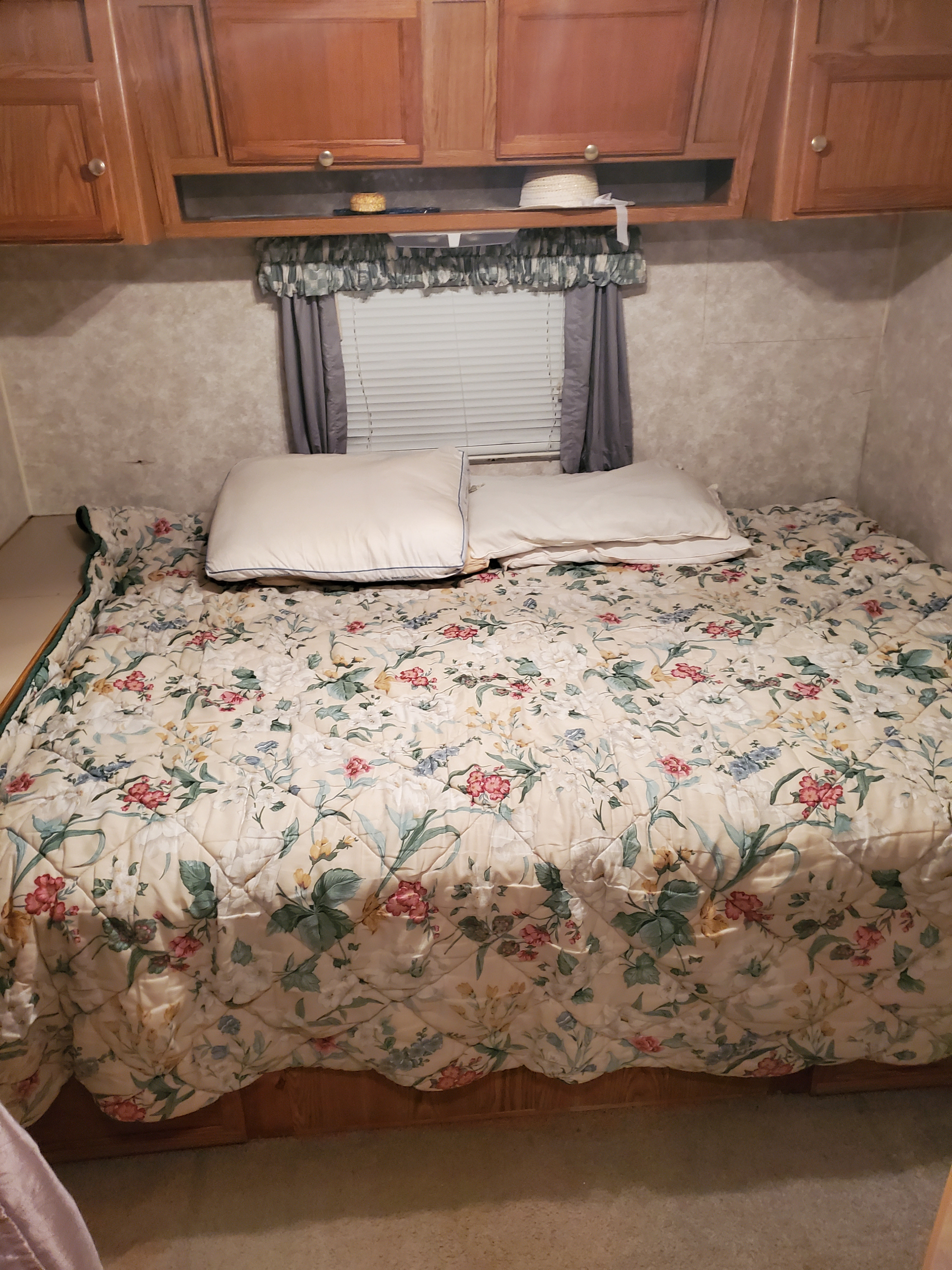 Cozy RV rental bedroom features a floral comforter on bed, pillows, wooden cabinets & window.. R-Vision Trail-Lite 2000