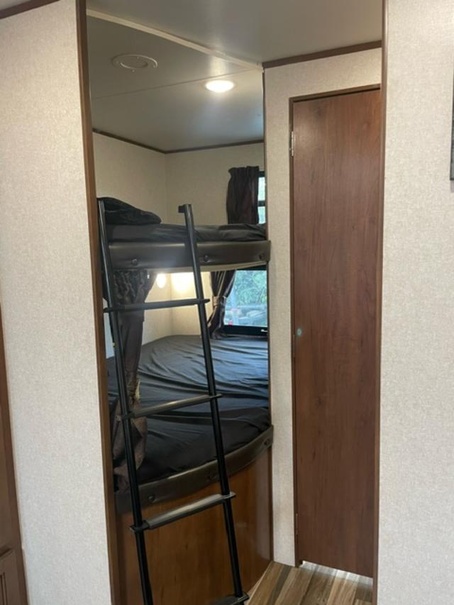 RV rental with bunk beds and ladder. Dark bedding, window, and a wooden door define this compact sleeping area.. Jayco Jay Flight 2017