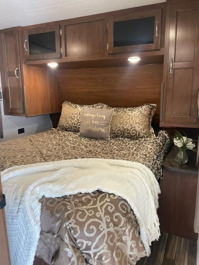 Cozy RV rental bedroom featuring a full bed with patterned bedding, overhead cabinets, and a decorative pillow.. Jayco Jay Flight 2017