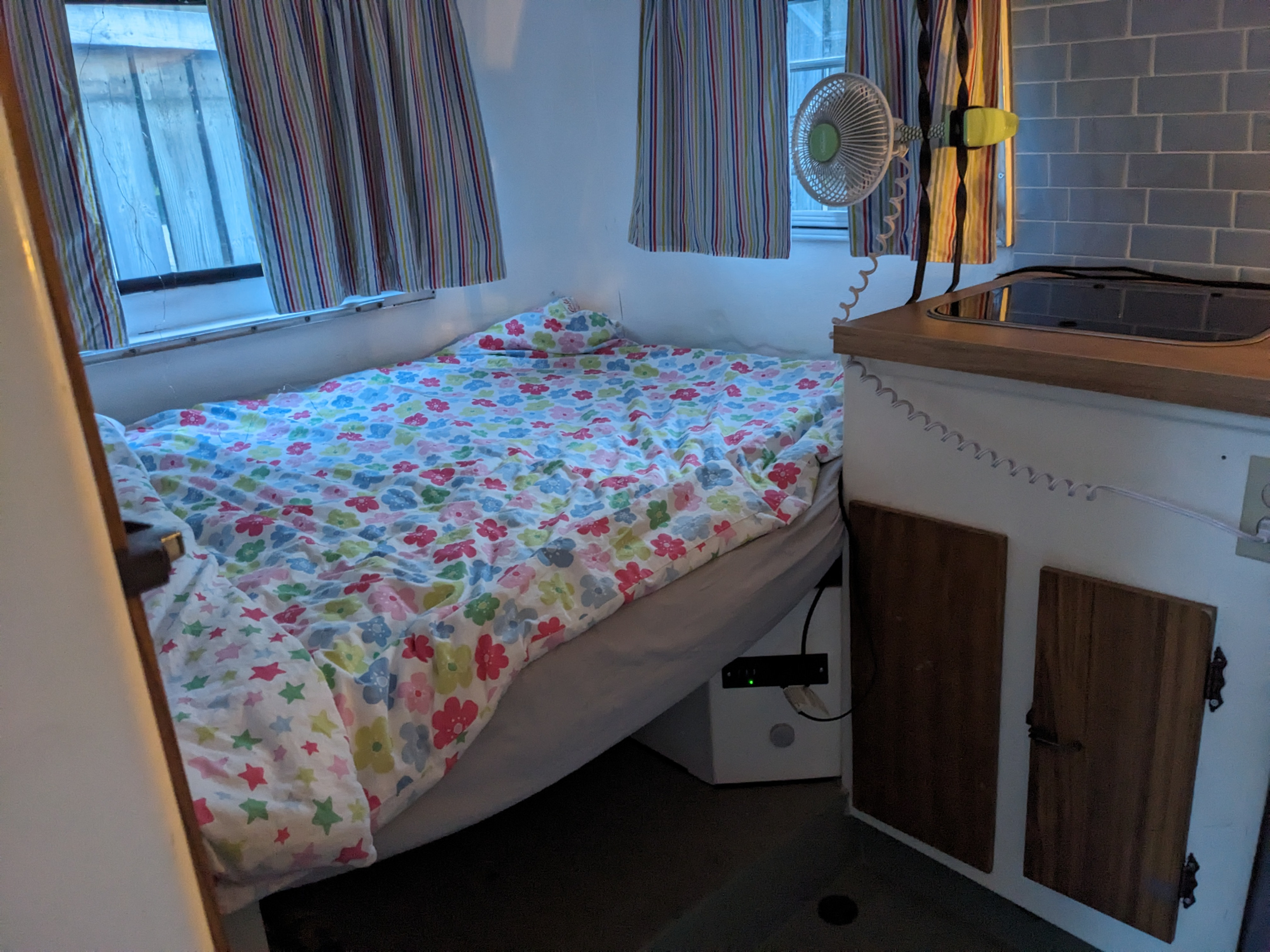 Cozy RV rental interior with a comfy floral bed, windows with striped curtains, and a compact kitchen. Ideal for travel!. Boler Boler 1300 1974