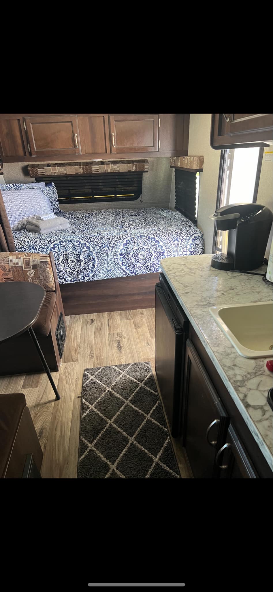 Cozy RV rental interior with a patterned bed, compact kitchen, and dinette. Ideal for comfortable travel.. Jayco Jay Flight 2018
