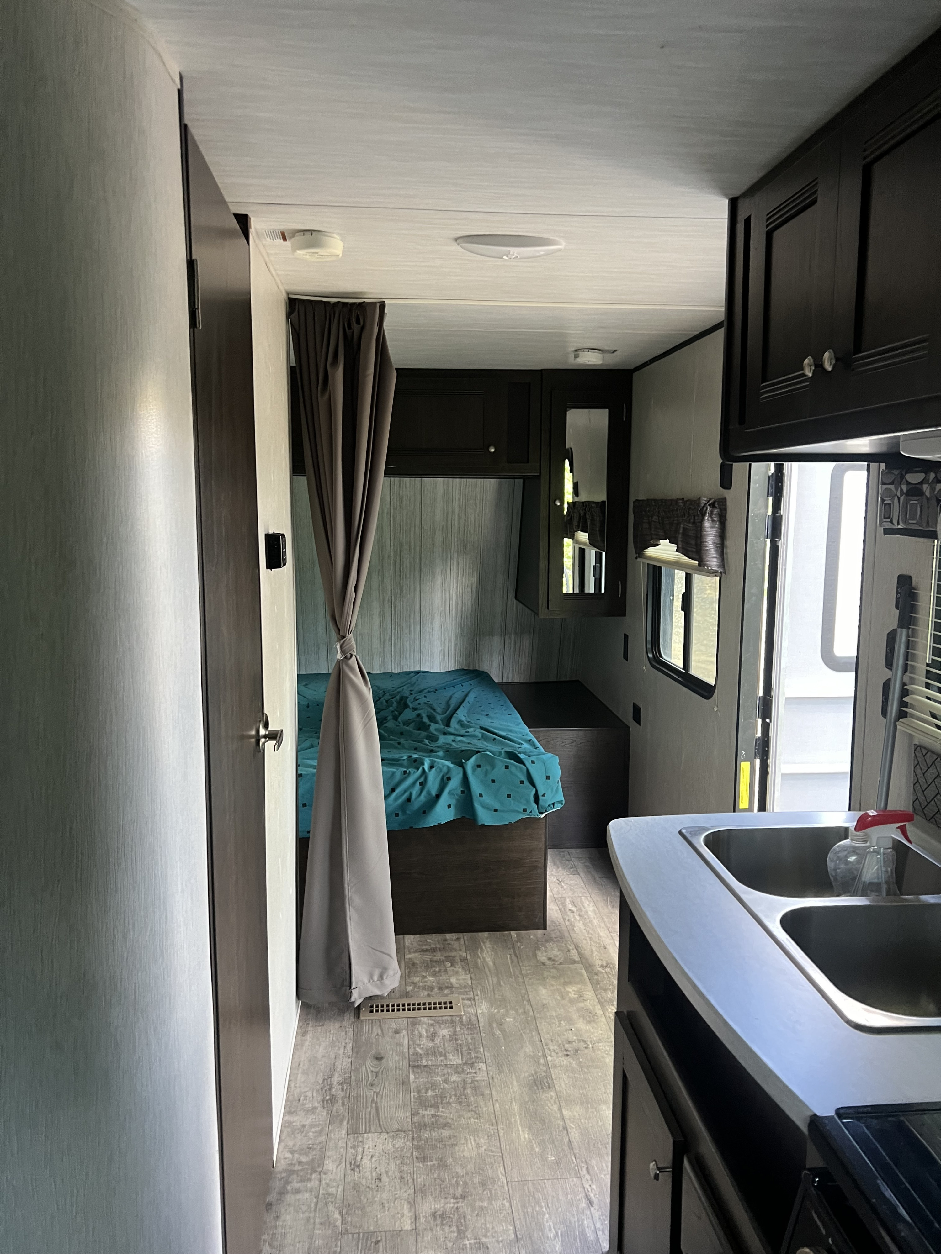 Cozy RV rental interior: kitchen with sink & dark cabinets leads to a bedroom area with a bed and privacy curtain. Ideal for travel.. Heartland RVs Pioneer 2020