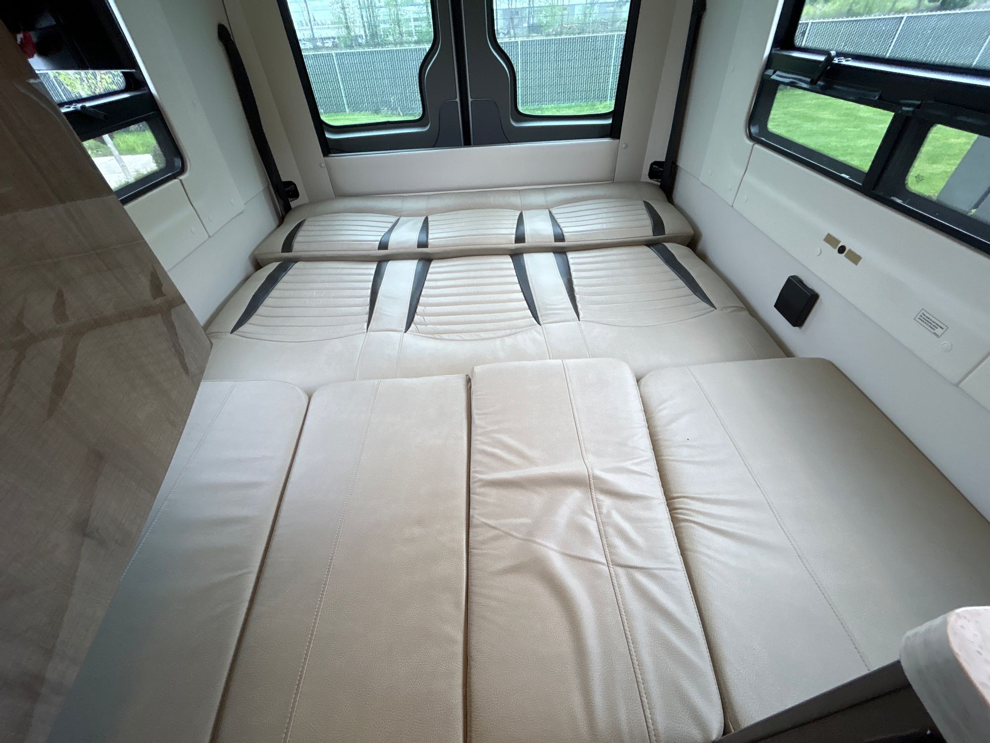 Inside this RV rental: a spacious, light beige convertible bed with quilted sections. Windows offer a view of greenery outside.. Winnebago Era 2016